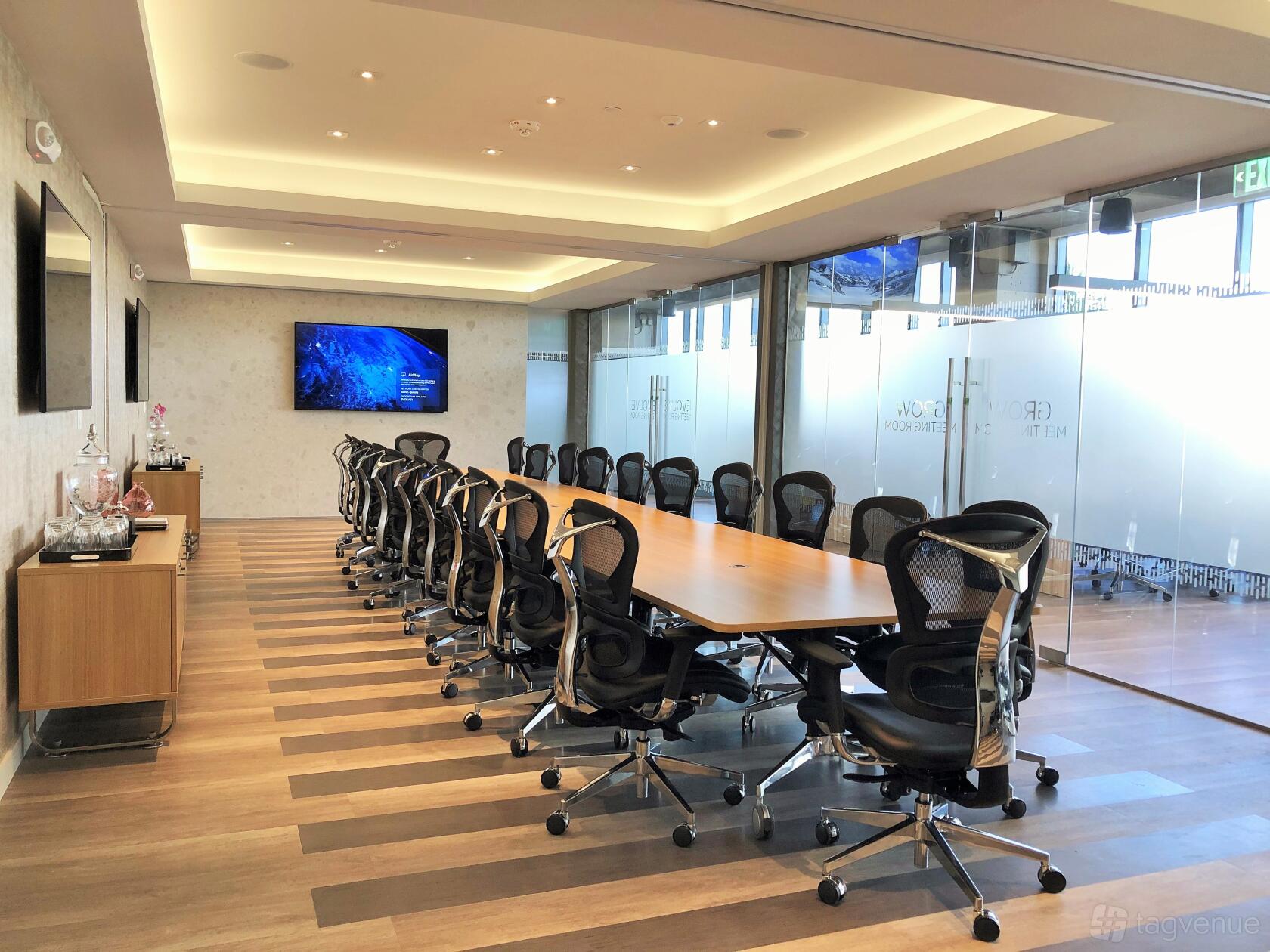 A meeting room with a long wooden conference table, ergonomic chairs, and floor-to-ceiling windows at Iconic Workspaces @ Aventura.