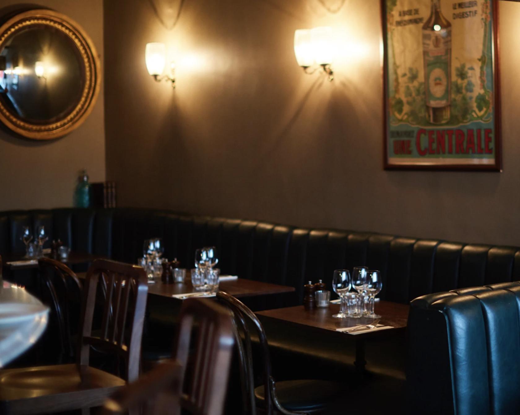 A dining room with tufted leather banquette seating, wooden tables, and wall-mounted lighting at Patron Restaurant.