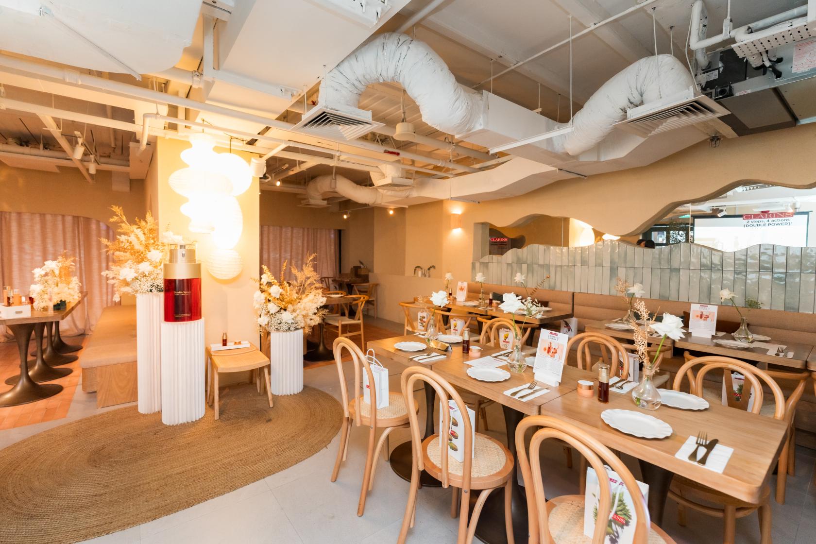 A restaurant with light wood chairs, round tables, dried floral arrangements, and curved mirrored walls at Ela Jalan Sultan.