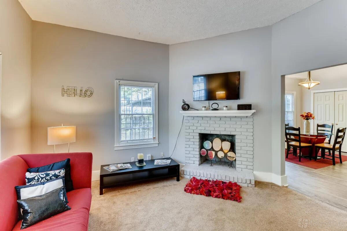 An apartment living room with a white brick fireplace, wall-mounted TV, and red sofa at Historic Westend Intown Duplex Apartment.