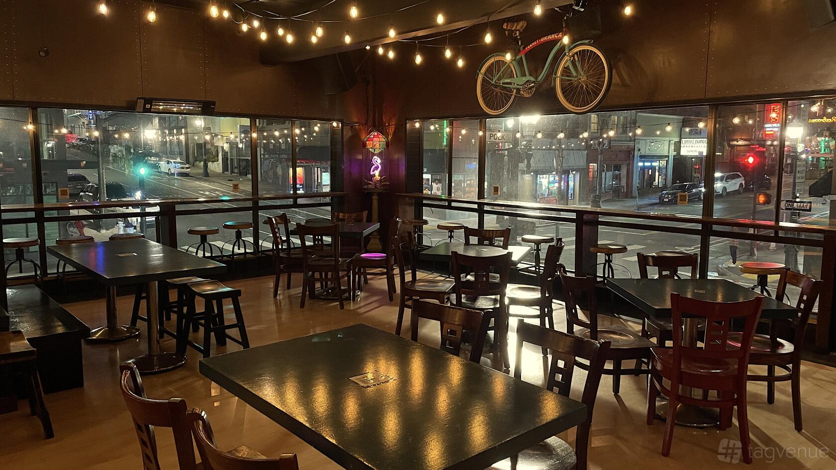 A function room in a bar with string lights, large street-facing windows, and wooden tables and chairs at Upcider.