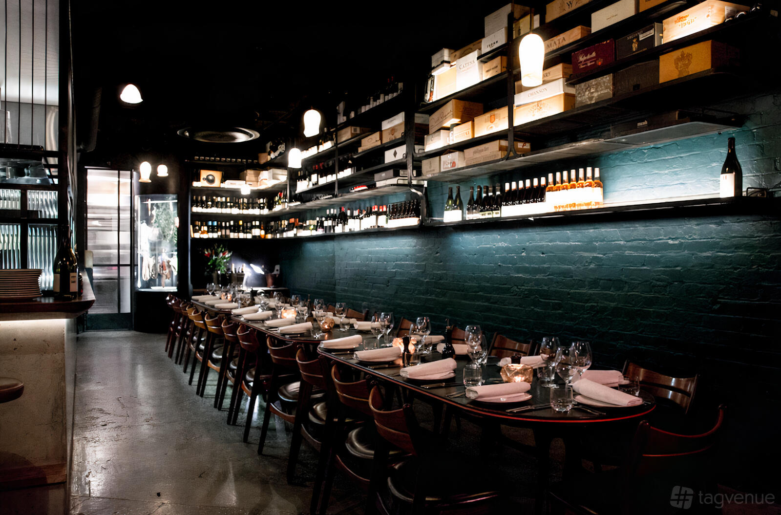 An event space in a bar with long dining tables, wine bottle displays, and exposed brick walls at Juliet Melbourne.
