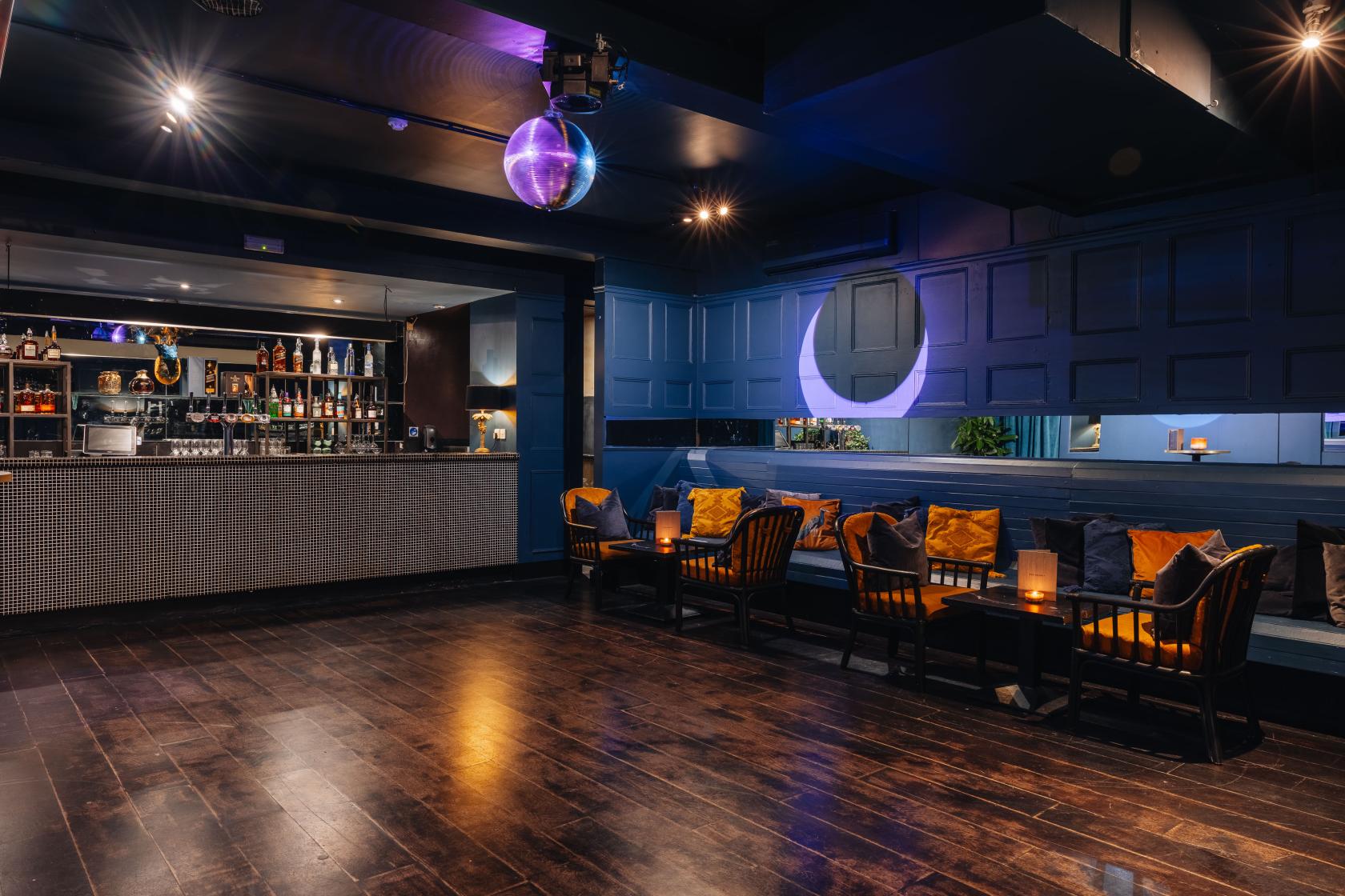 A function room with dark wood floors, a mirrored disco ball, and a built-in bar at Exhibit.