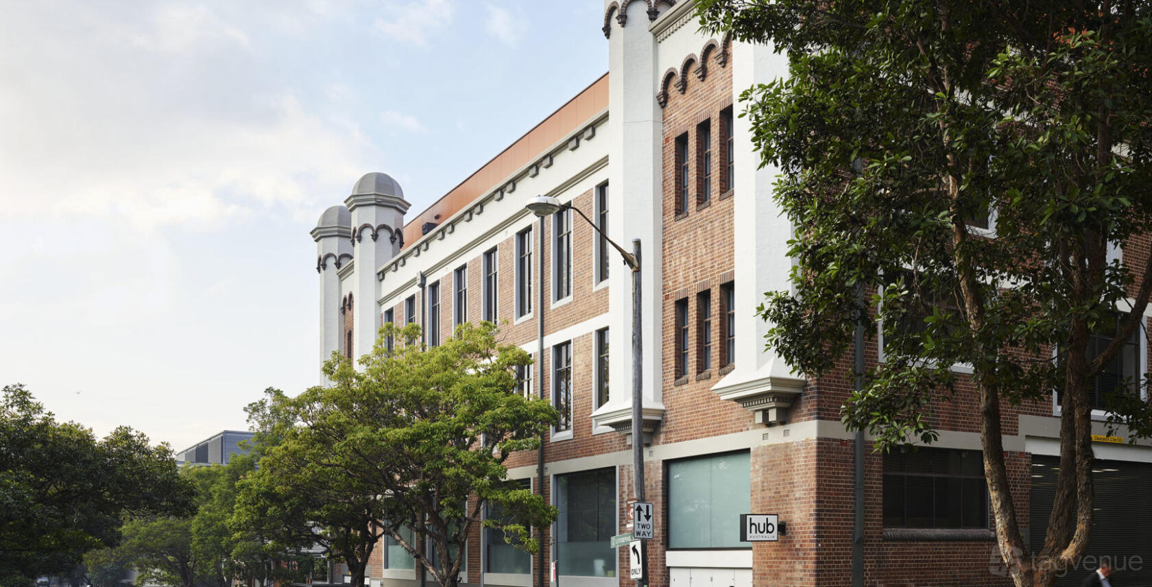 A coworking space with a red brick facade, large arched windows, and leafy trees at Hub Hyde Park.