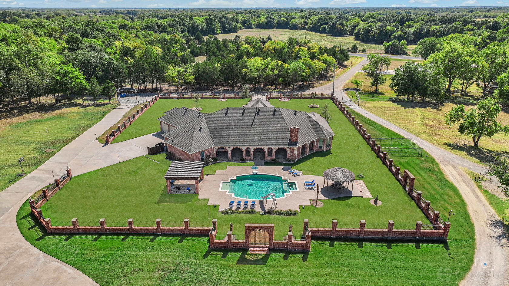 A ranch venue with a large brick building, sprawling fenced lawn, and central outdoor pool at The Dream Ranch.