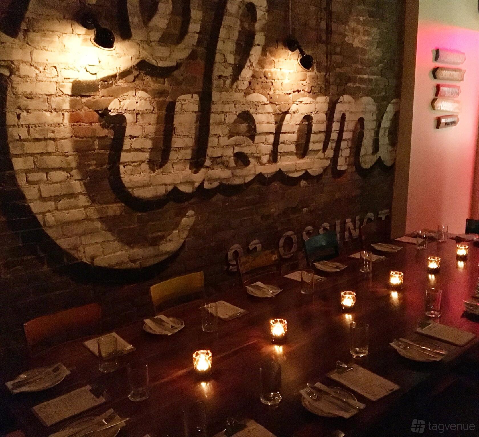 A restaurant with exposed brick walls, painted mural, and a long wooden table with candlelight at La Cubana - OSSINGTON VILLAGE.