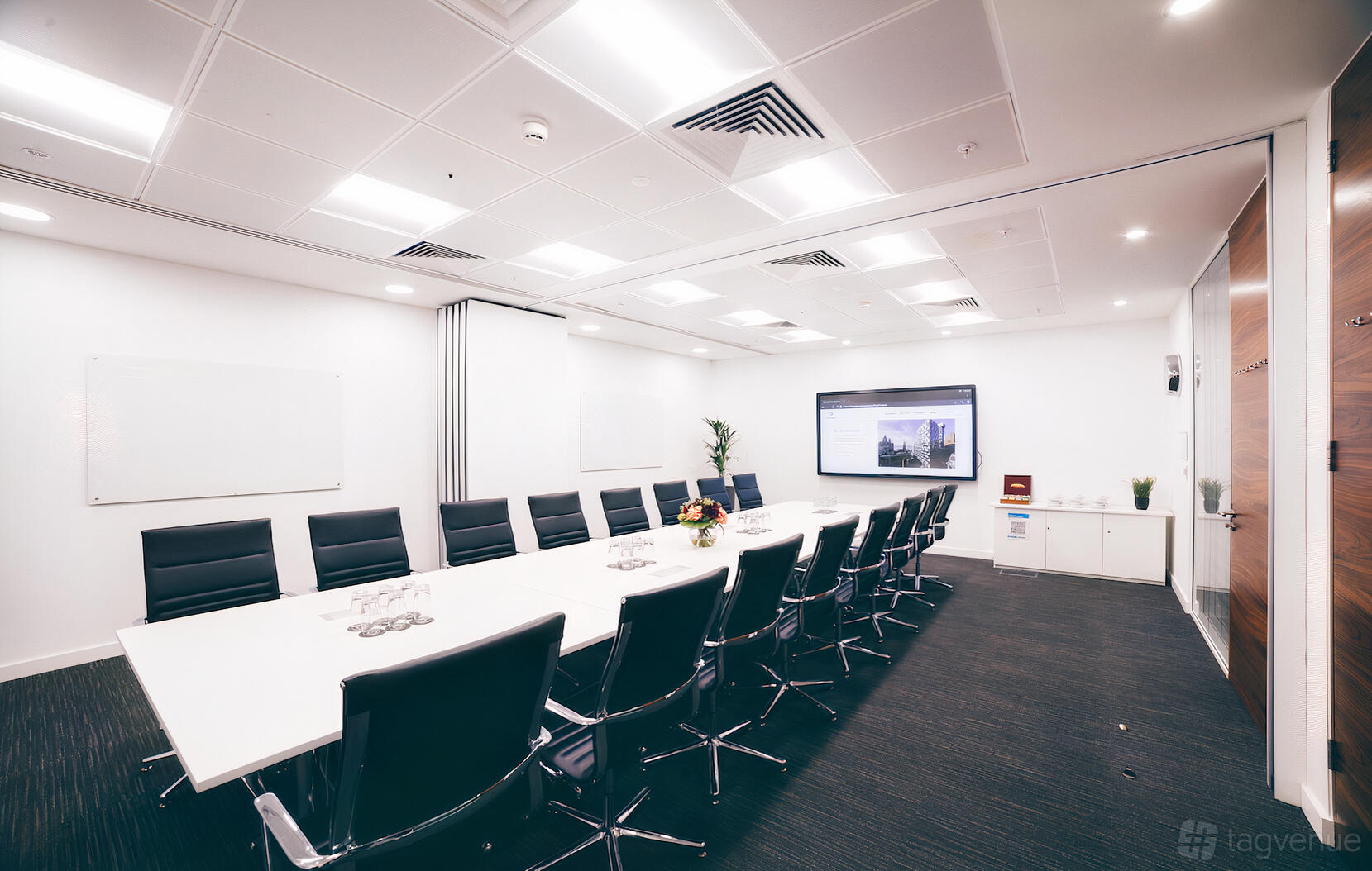 A boardroom with a long white table, black leather chairs, wall-mounted screens, and whiteboards at Orega Liverpool.