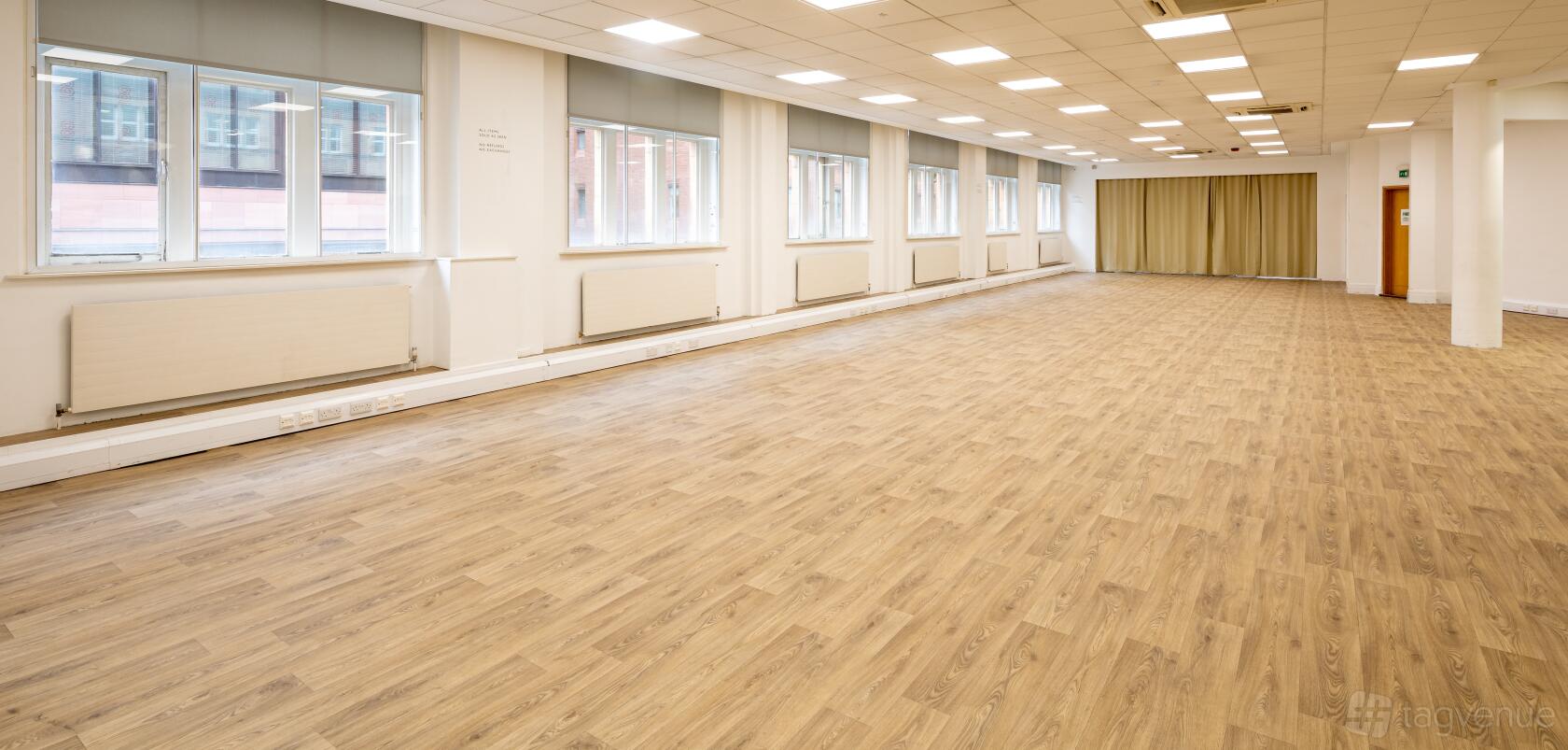 An event venue with large windows, wood-style flooring, and ceiling panel lights at The Music Room.