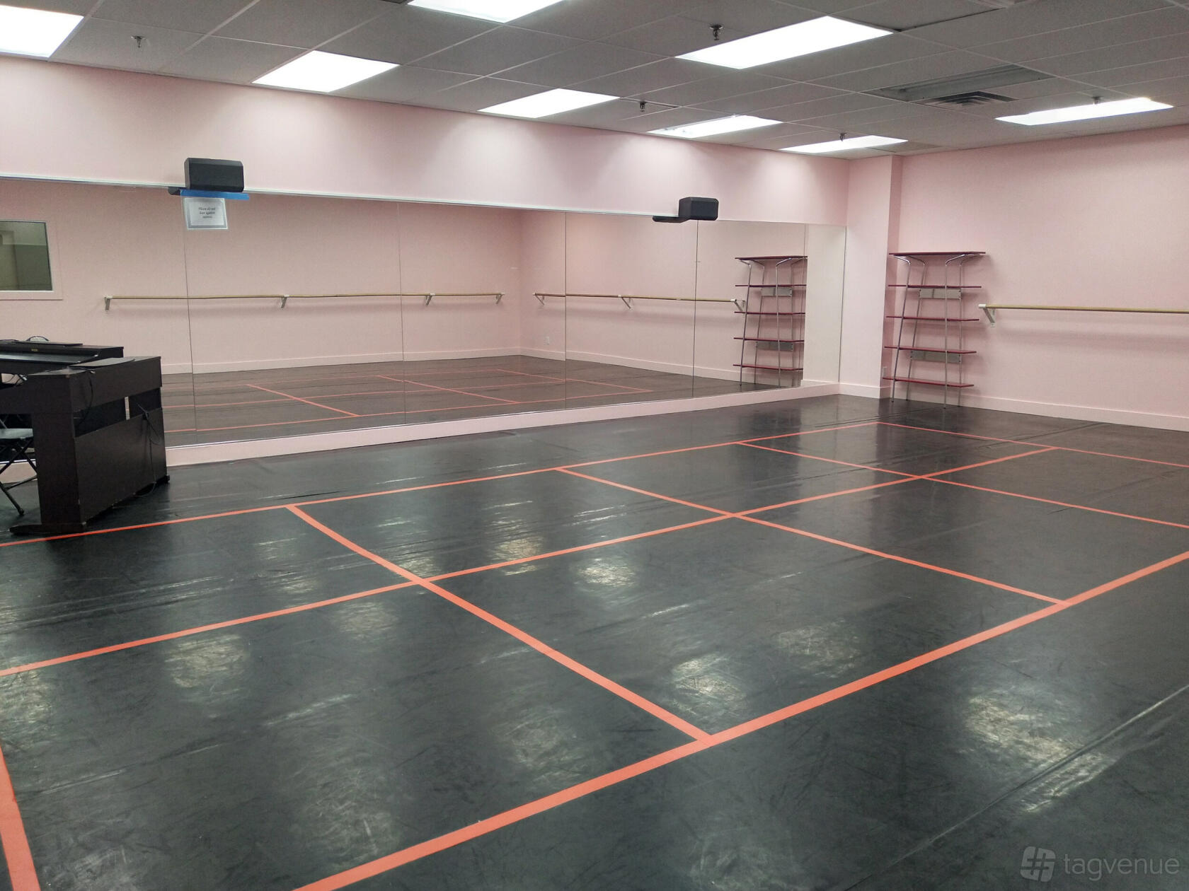 A dance studio with mirrored walls, ballet barres, and a black marley floor with orange grid lines at Martha Hicks School Of Ballet.