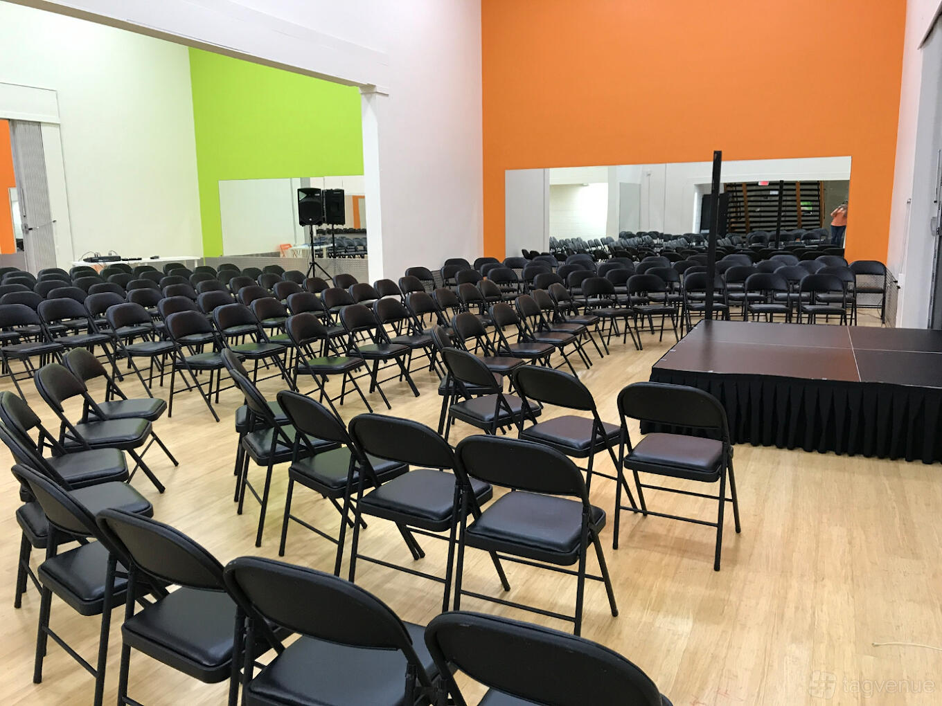 An event space with folding chairs facing a small stage, hardwood floors, and large wall mirrors at Academy of Creative Arts.