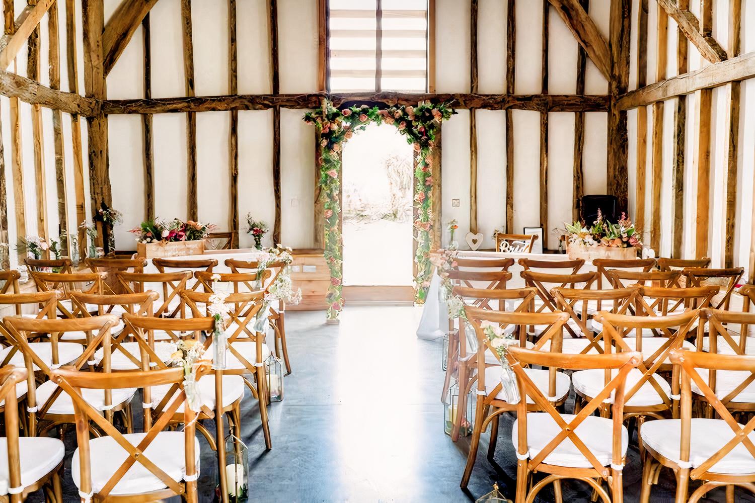 A barn venue with exposed timber beams, whitewashed walls, and wooden chairs arranged for a ceremony at Rowley Barn.