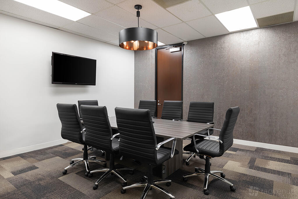 A boardroom with a rectangular table, eight black leather chairs, a wall-mounted TV, and a pendant light at Premier Workspaces - El Segundo.