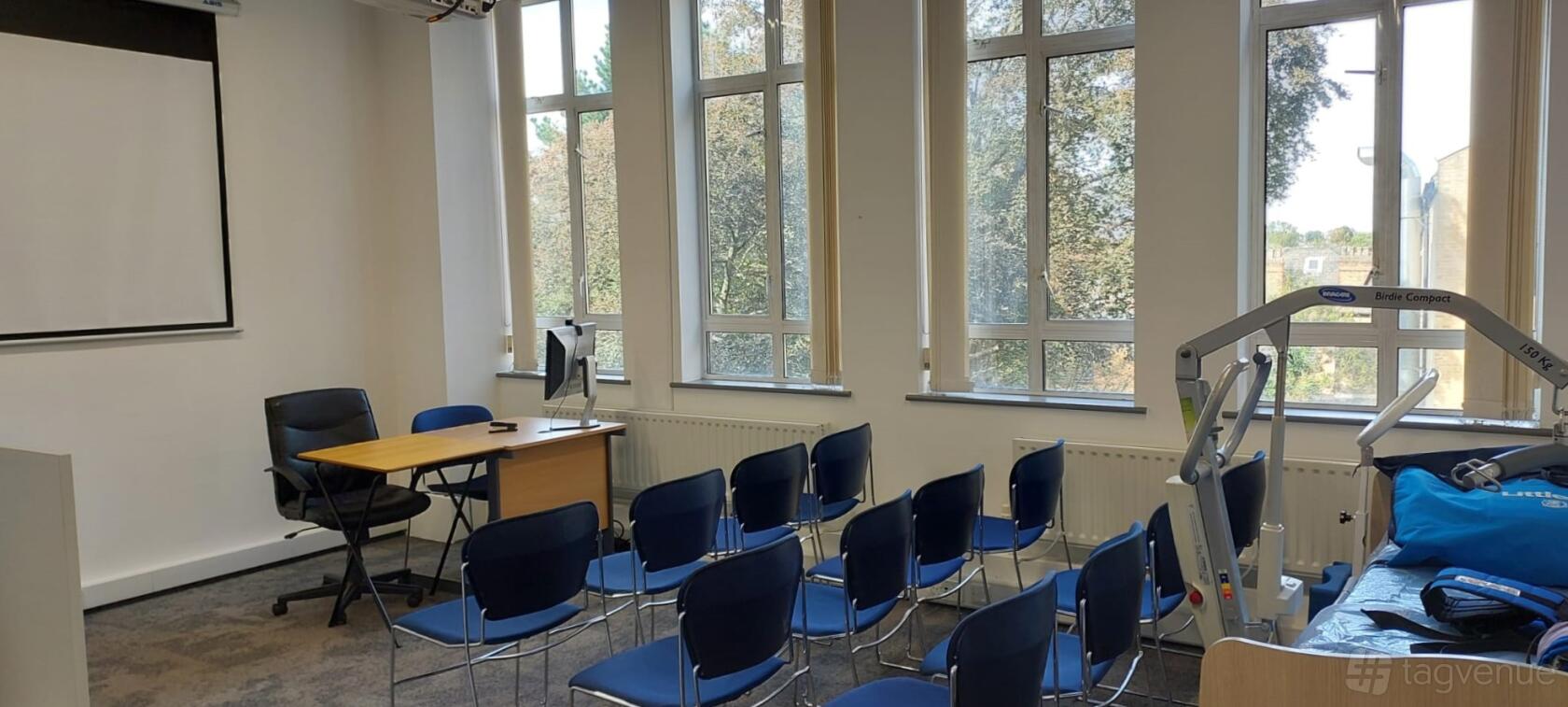 A meeting room with rows of blue chairs, a wooden desk, and large windows at Rhythmic Skills.
