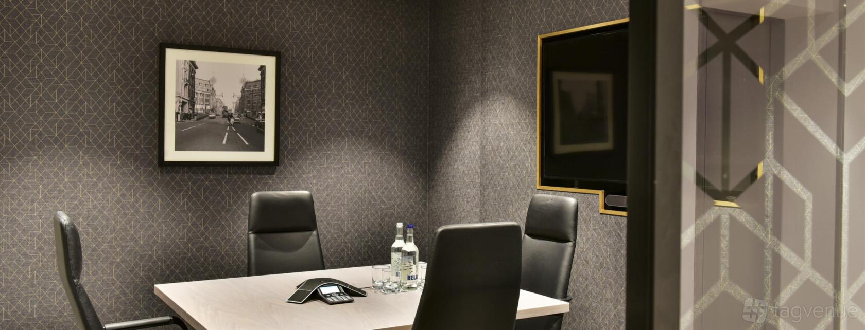 A meeting room with dark textured walls, a wall-mounted screen, and a table set with water bottles at 288 Bishopsgate.