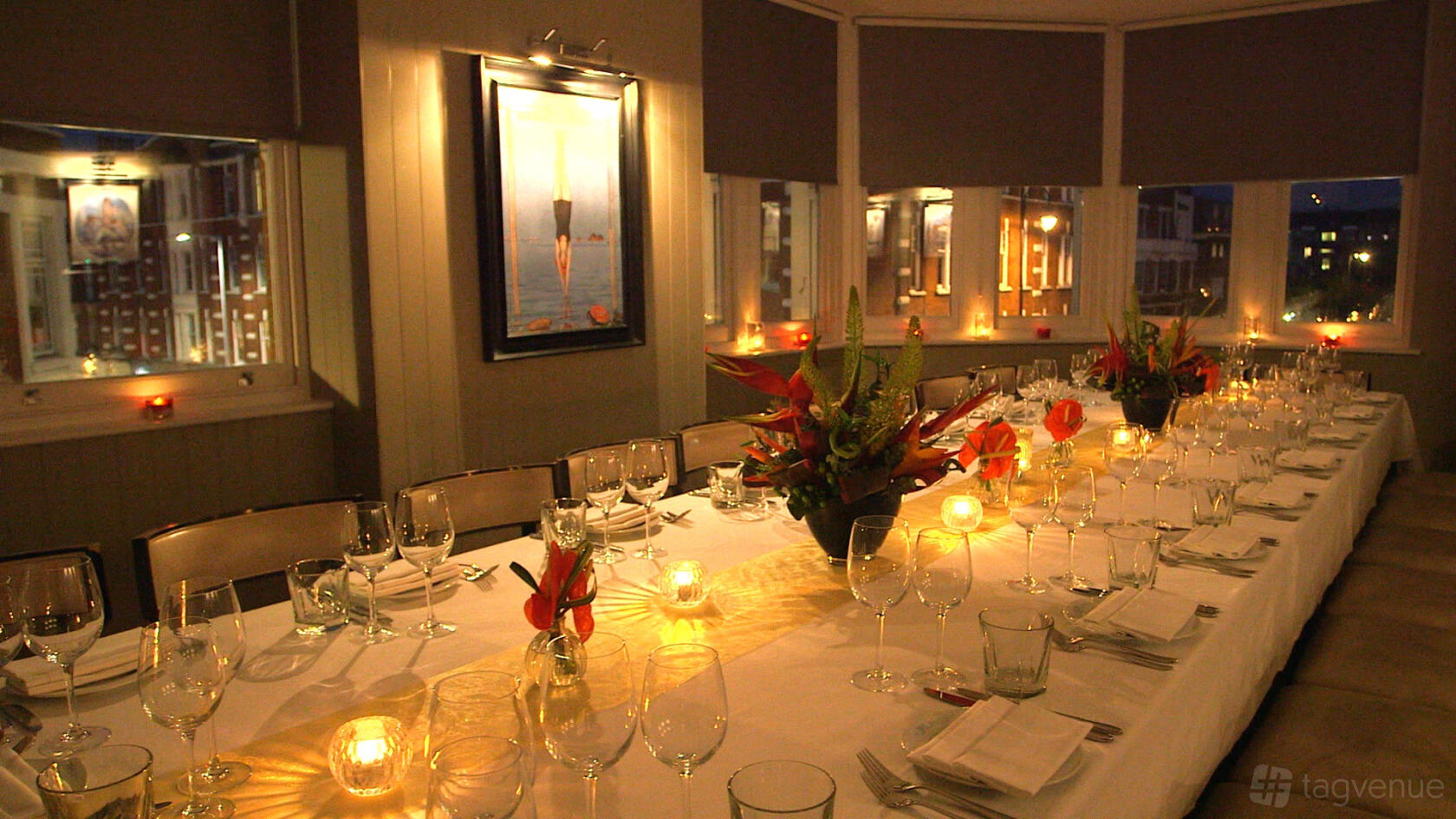 An event space in a cocktail bar with a long dining table, candlelight, floral centerpieces, and large windows at Albert's at Beaufort House.