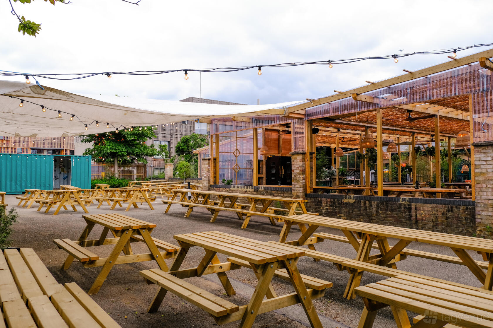 An outdoor pub area with wooden picnic tables, string lights, and covered seating at Pacific Tavern.
