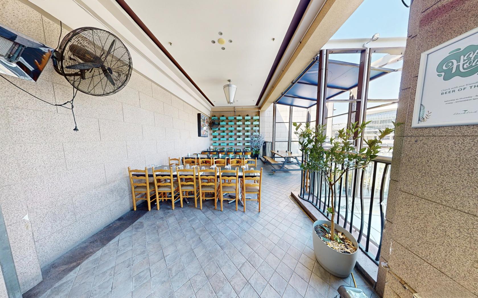 An outdoor dining area with wooden chairs, potted plants, and wall-mounted fans at Blackbird Cafe.