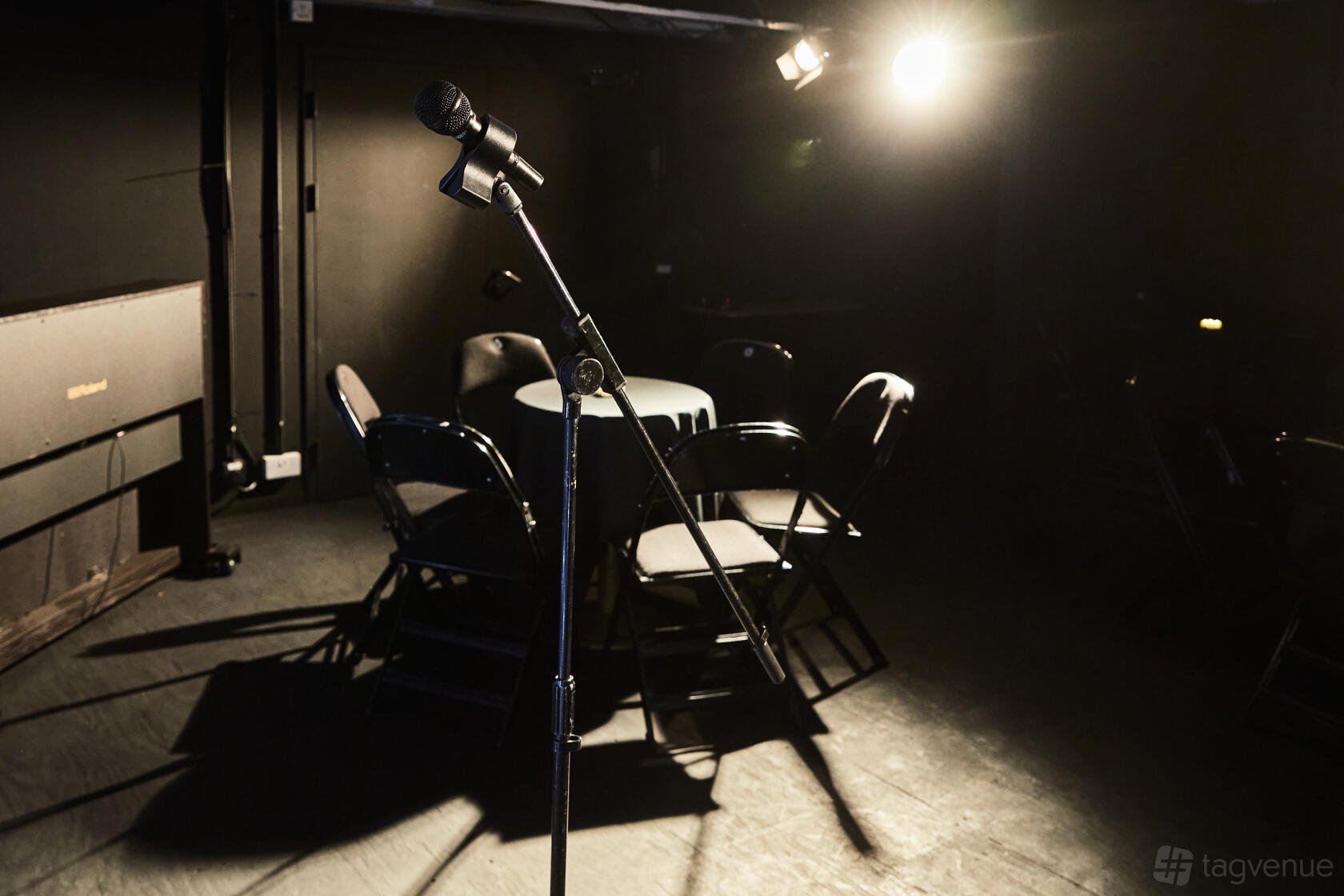 An event space in a theatre with a microphone on stage, round table, and folding chairs at Seven Dials Playhouse.