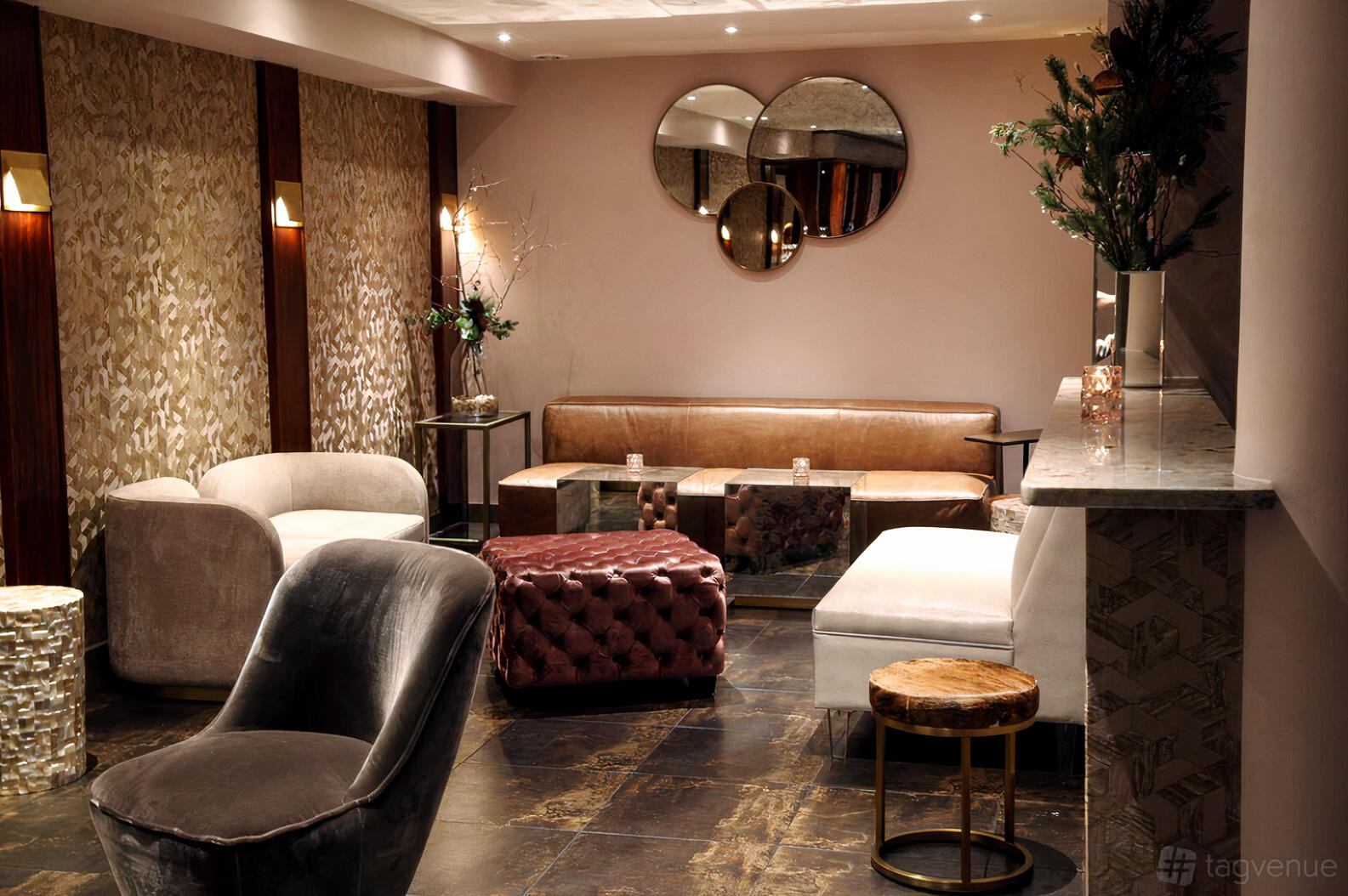 A dining room with velvet armchairs, a tufted ottoman, patterned wallpaper, and round wall mirrors at Yara.