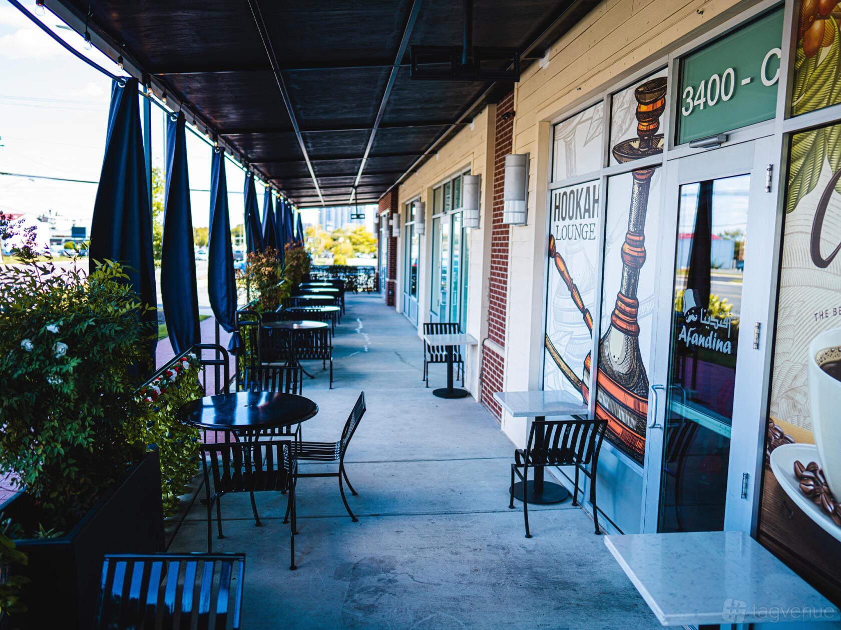 An outdoor patio at AFANDINA HOOKAH LOUNGE with black metal tables and chairs along a covered walkway.