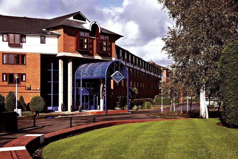 A hotel exterior with red brick facade, large windows, and a blue canopy entrance at Copthorne Hotel Manchester.