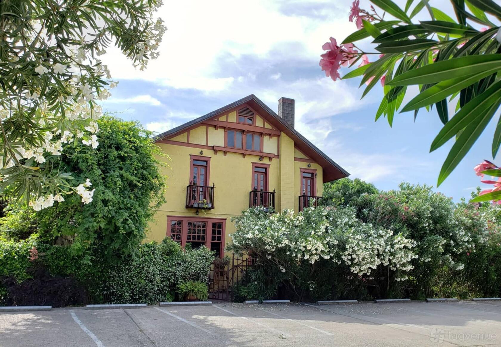 A historic building with yellow stucco walls, wooden trim, and lush greenery at AvantGarden.