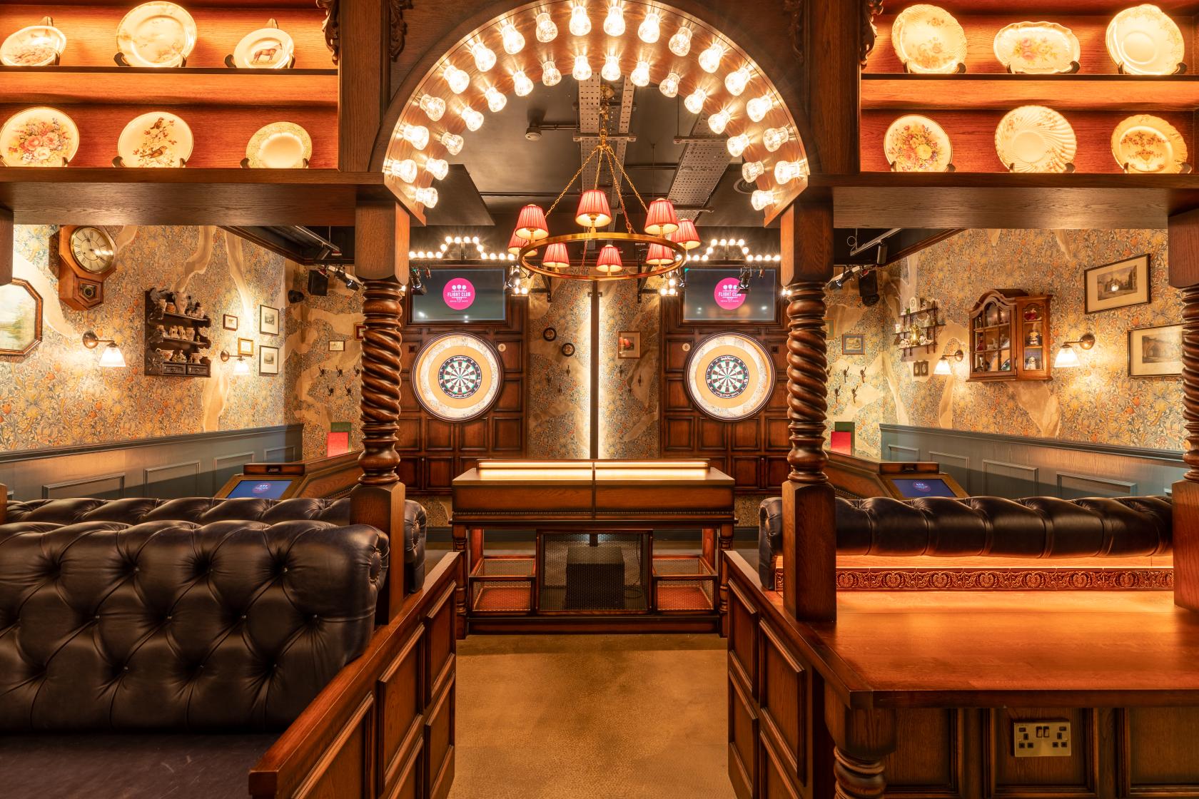 An event space in a bar with dartboards, tufted leather seating, vintage decor, and warm lighting at Flight Club Cheltenham.