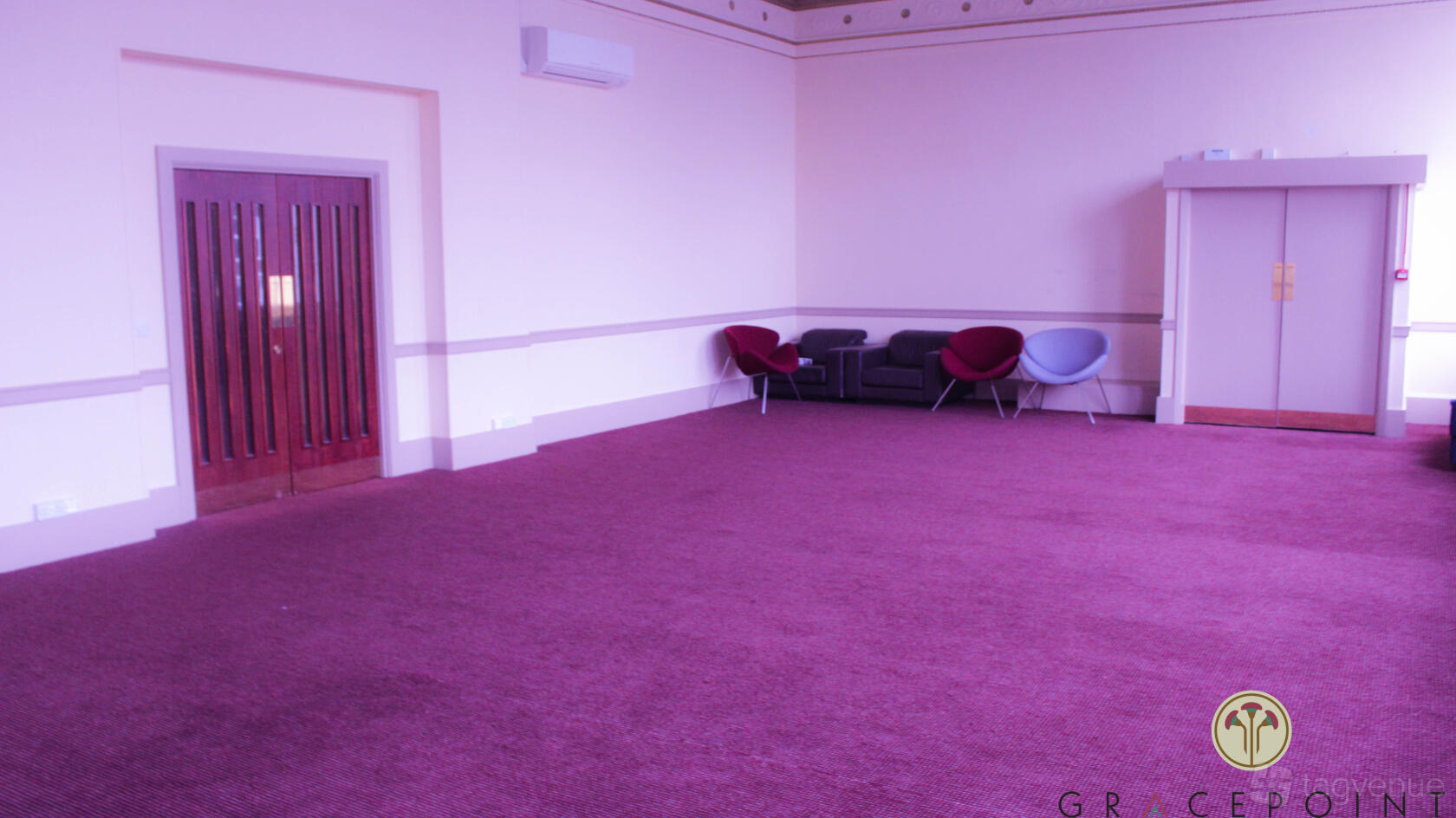 A meeting room with purple carpet, lounge chairs along the wall, and double wooden doors at Gracepoint.