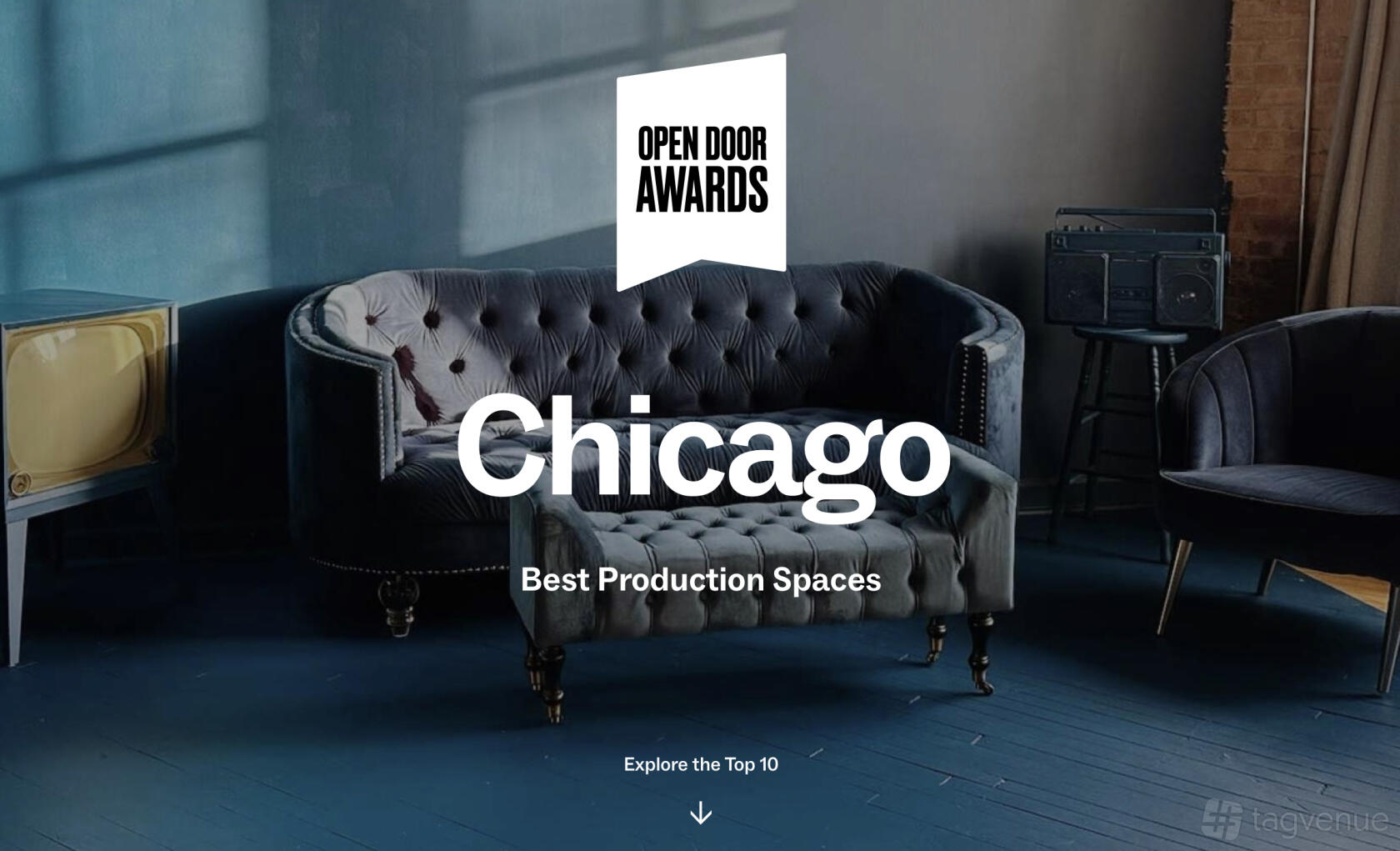 A photo studio with a vintage blue velvet sofa, dark wood floor, and textured exposed brick at Create at Upscale.