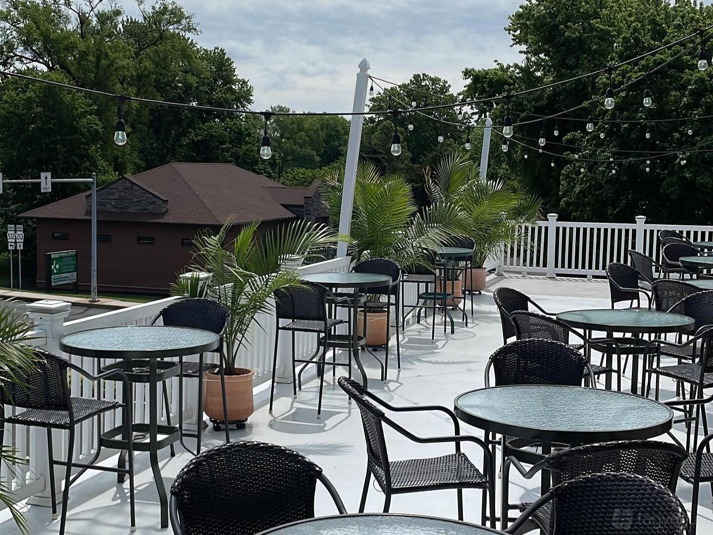 An outdoor terrace with round tables, black chairs, potted palms, and string lights at The Buck Hotel.