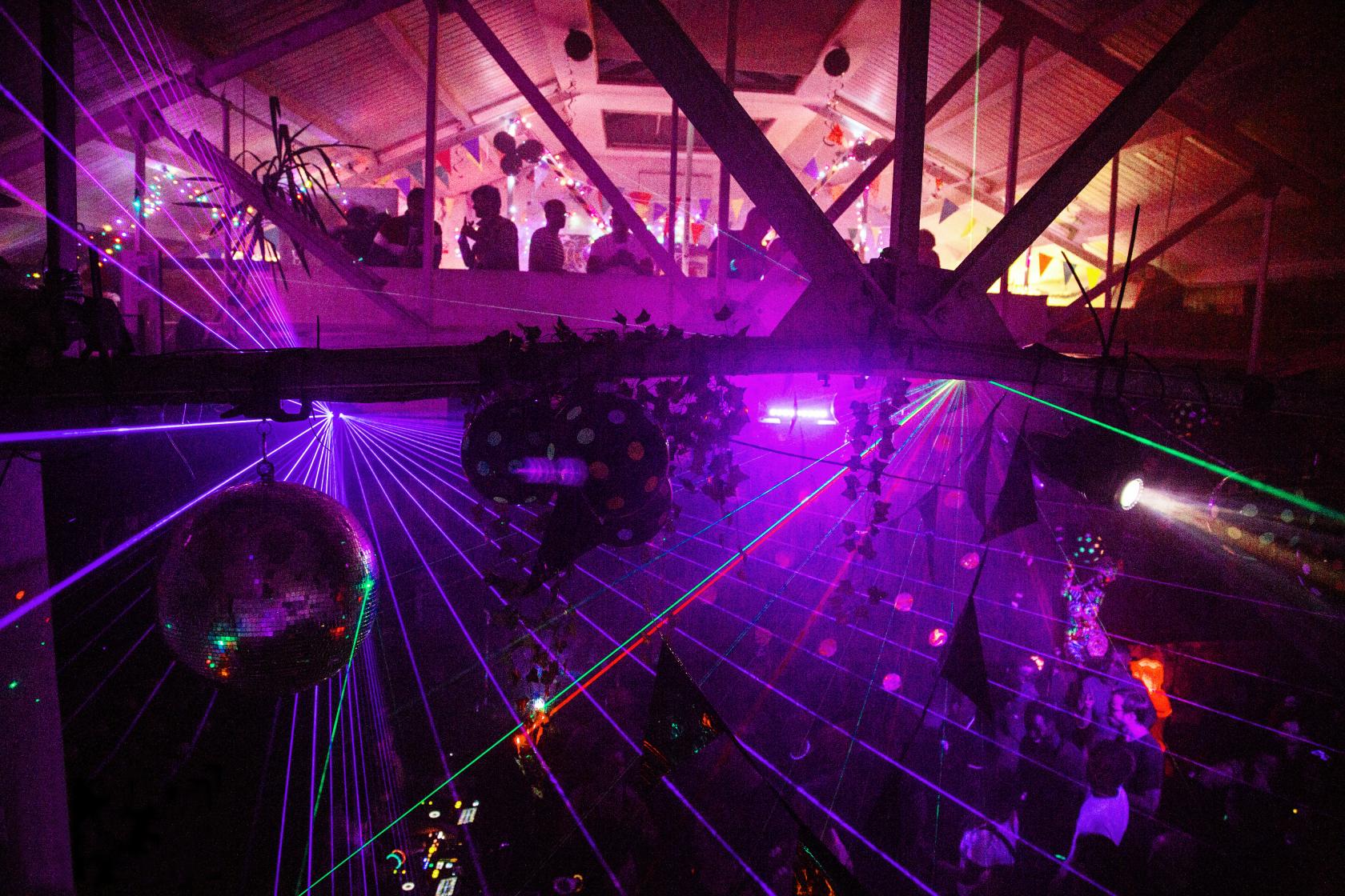 A nightclub loft with exposed beams, disco balls, and colorful laser lights at Low Profile Studios.
