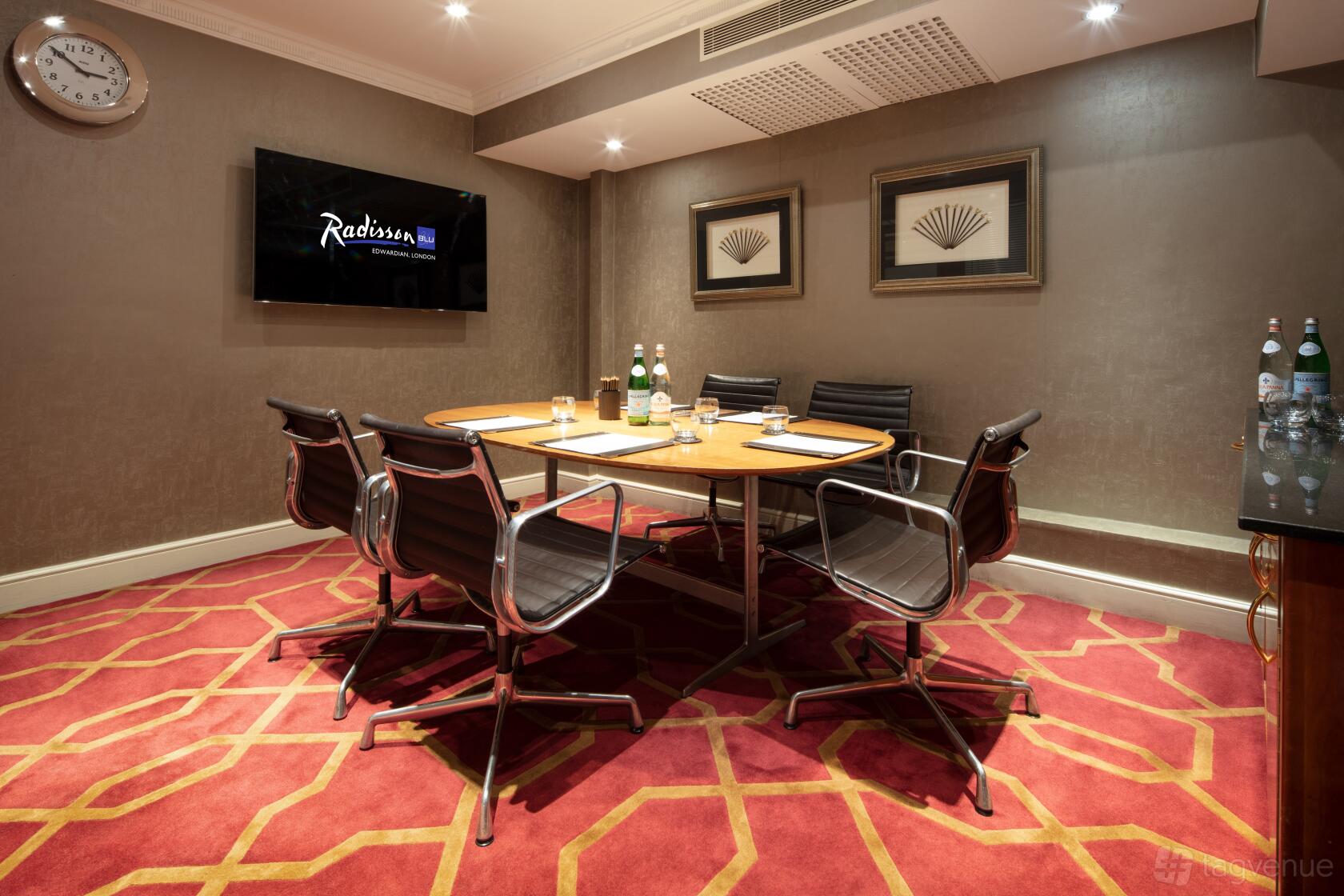 A meeting room with a rectangular wooden table, black leather chairs, and a wall-mounted screen at Radisson Blu Hotel, London Heathrow.