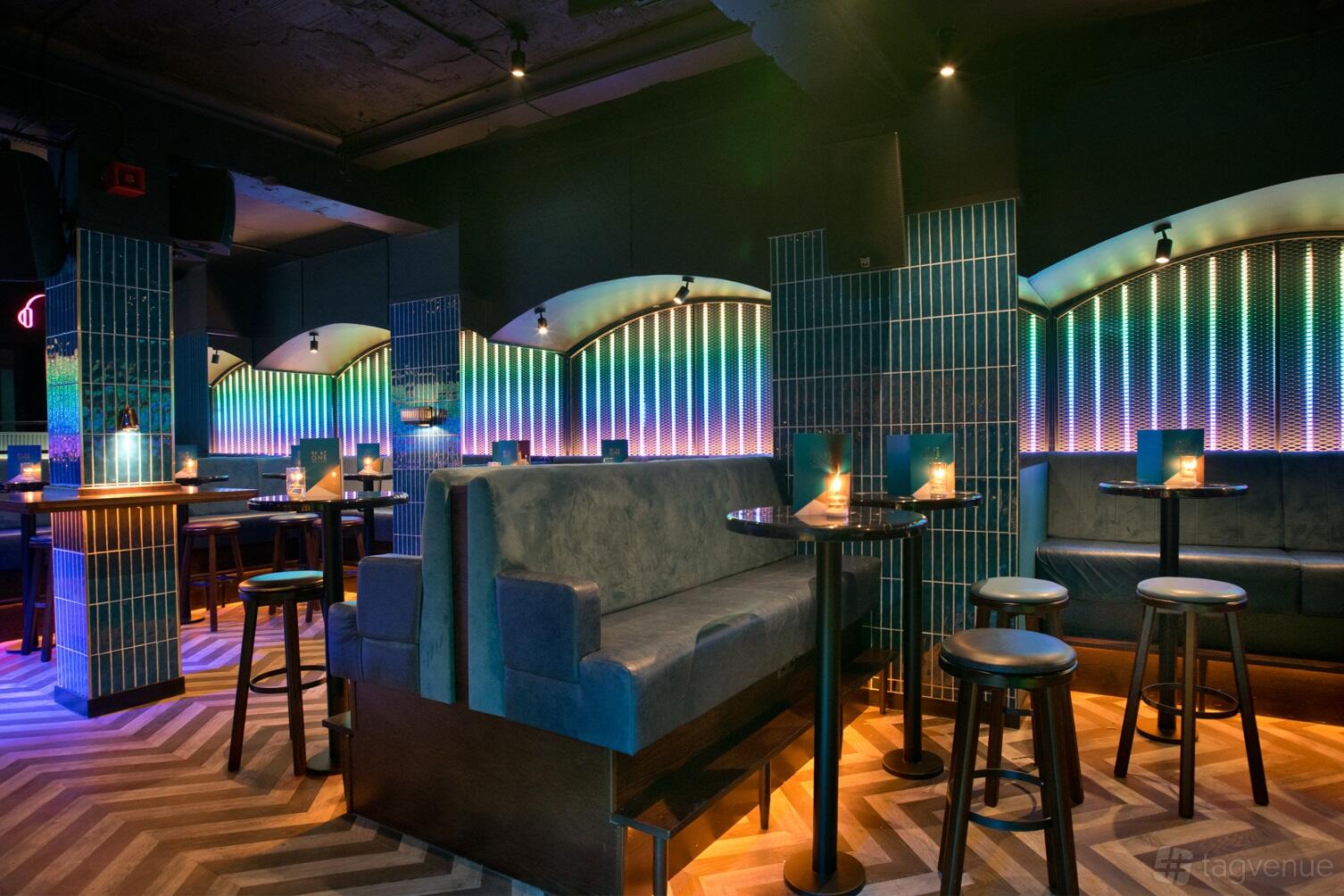 An event space with blue velvet booths, tall tables, and illuminated rainbow tile walls at Be at One Regent Street.