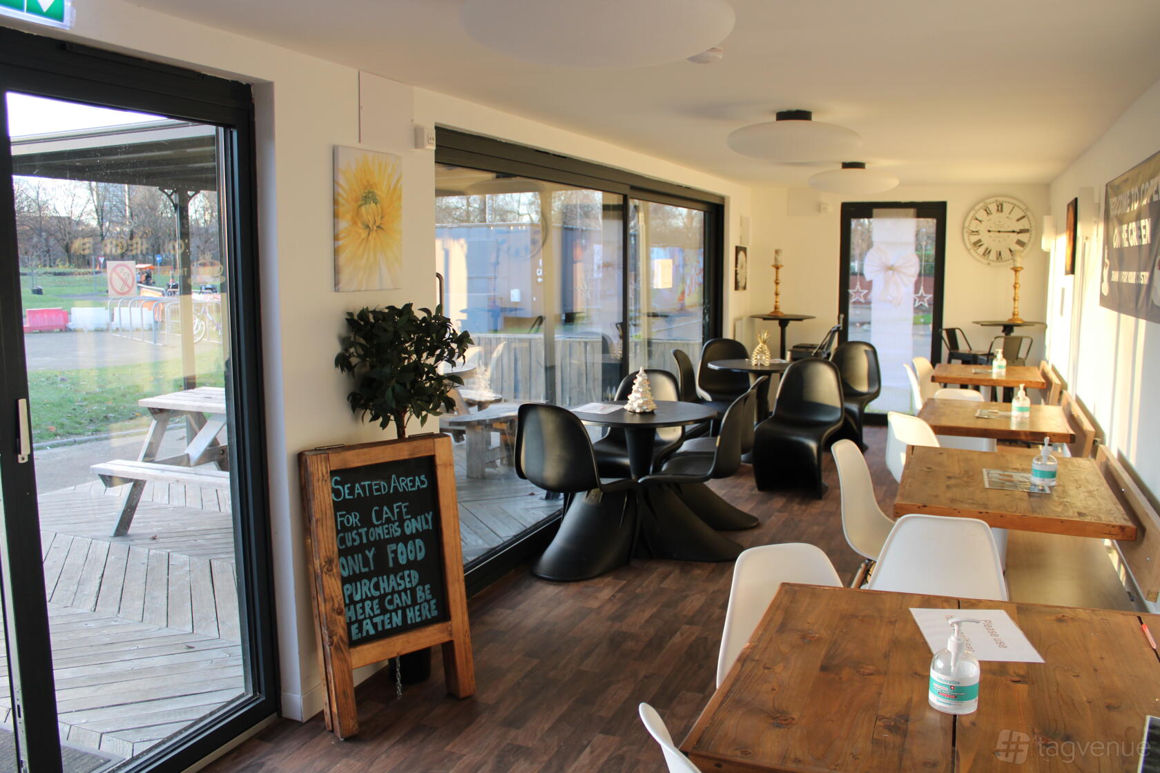 A cafe with large windows, wooden tables, modern black chairs, and outdoor seating at Coffee on the Green at Free Wheel North.
