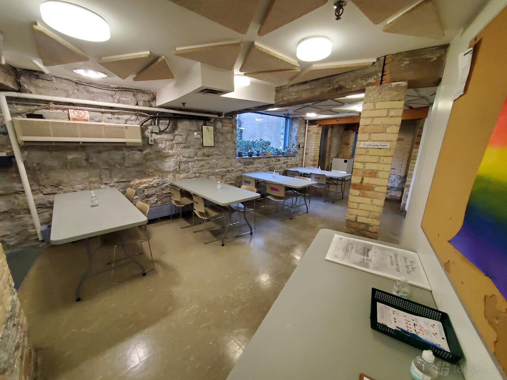 An event space with exposed brick walls, rectangular tables, and potted plants on the window sill at Cecil Community Centre.