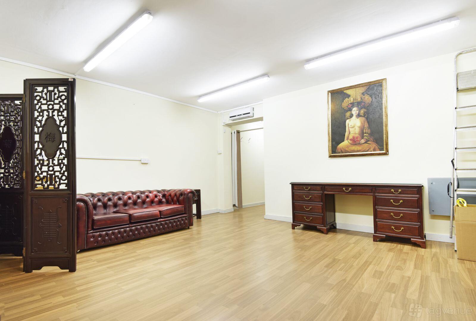 An art studio with wood flooring, a leather sofa, and a framed painting on the wall at Kang & Son.