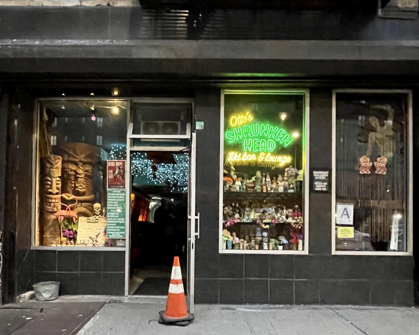A pub with large tiki statues and a neon sign in the front window at Otto's Shrunken Head.