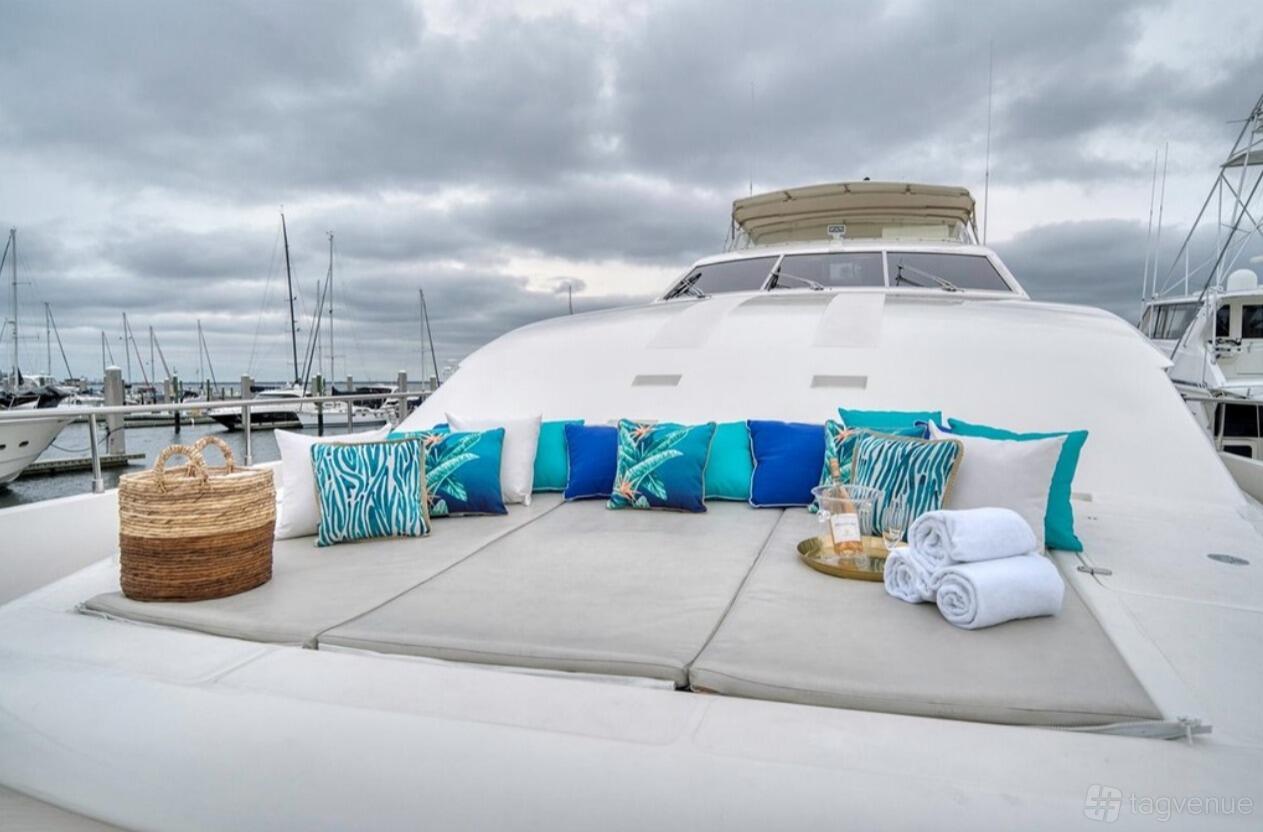 A luxury boat deck with cushioned sunbeds, patterned blue pillows, towels, and a wicker basket at Luxe Charters.