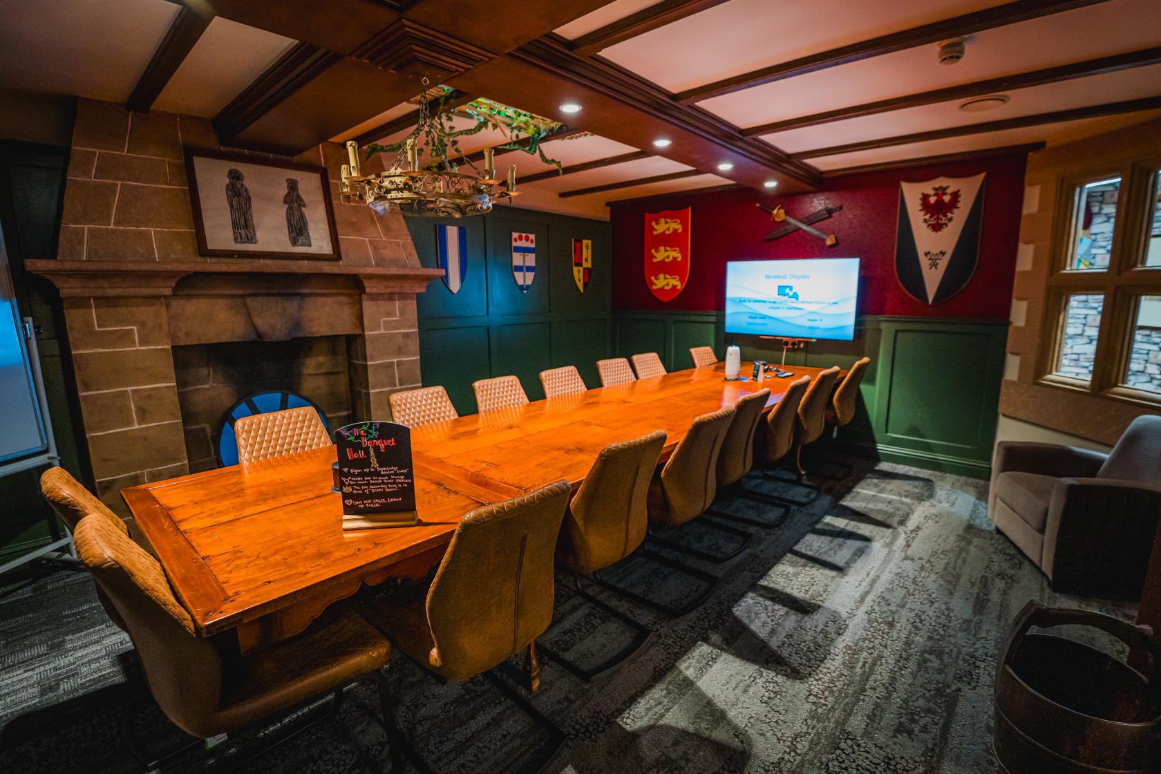 A boardroom with a long wooden table, high-back chairs, fireplace, and heraldic banners at DeskLodge Beacon Tower Bristol.