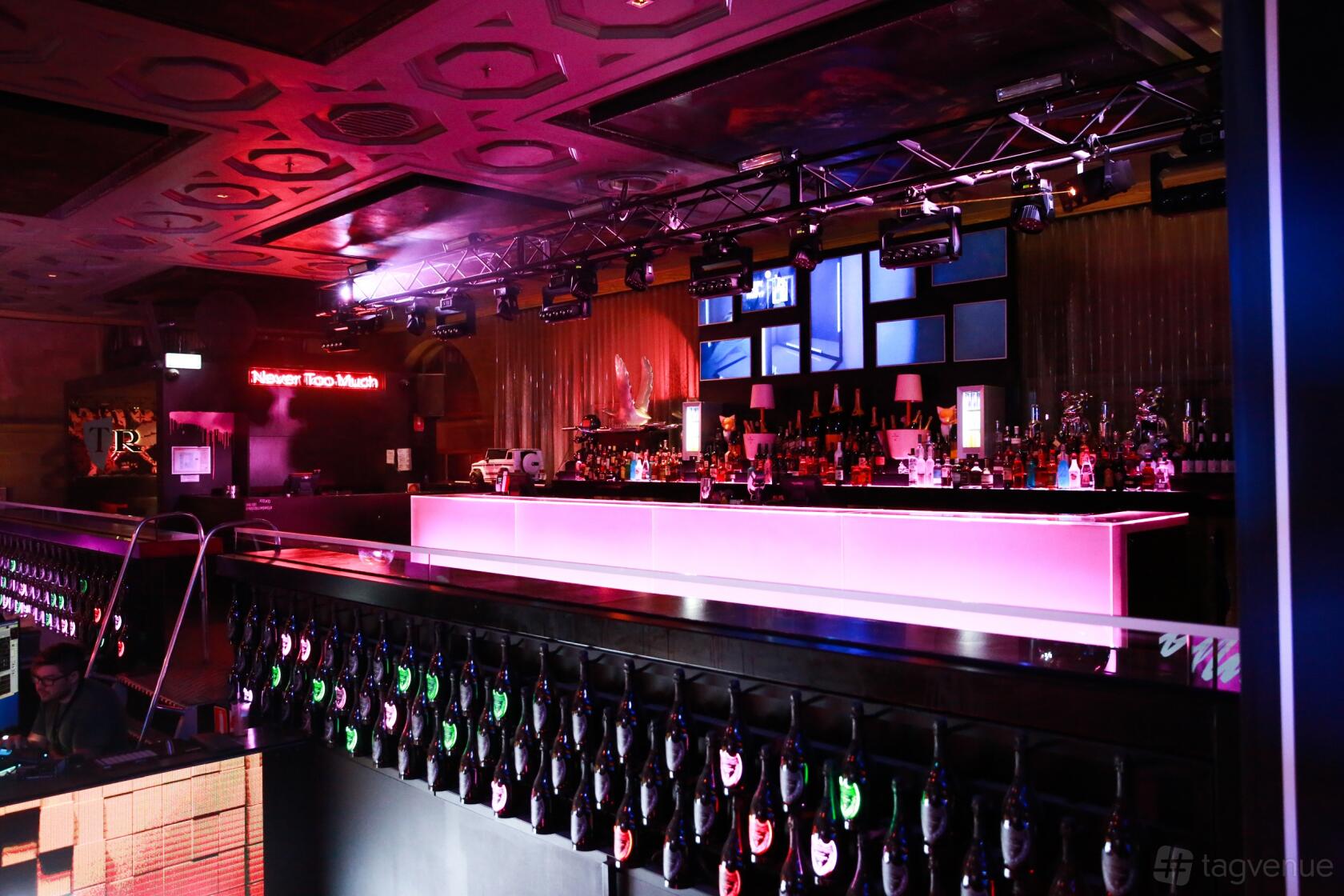 A nightclub with an illuminated bar counter, colorful lighting, and bottle-lined railing at Ms Collins.