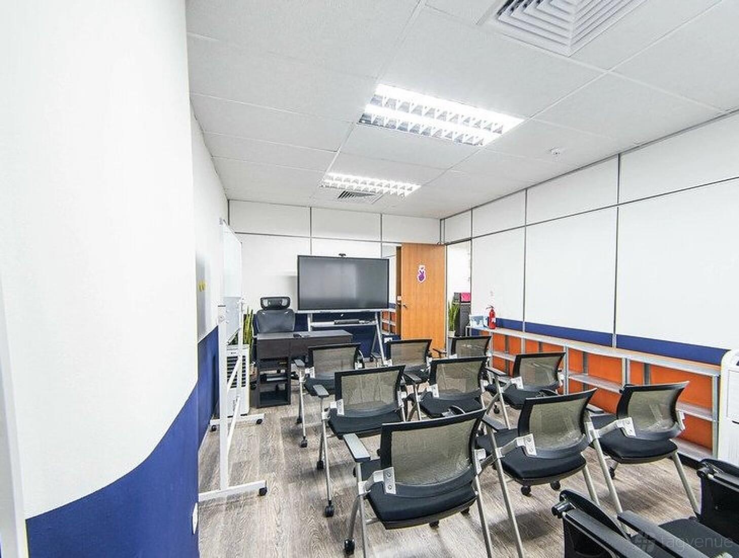 A classroom with mesh chairs arranged in rows, a large TV screen, and whiteboard walls at CuriousCore.