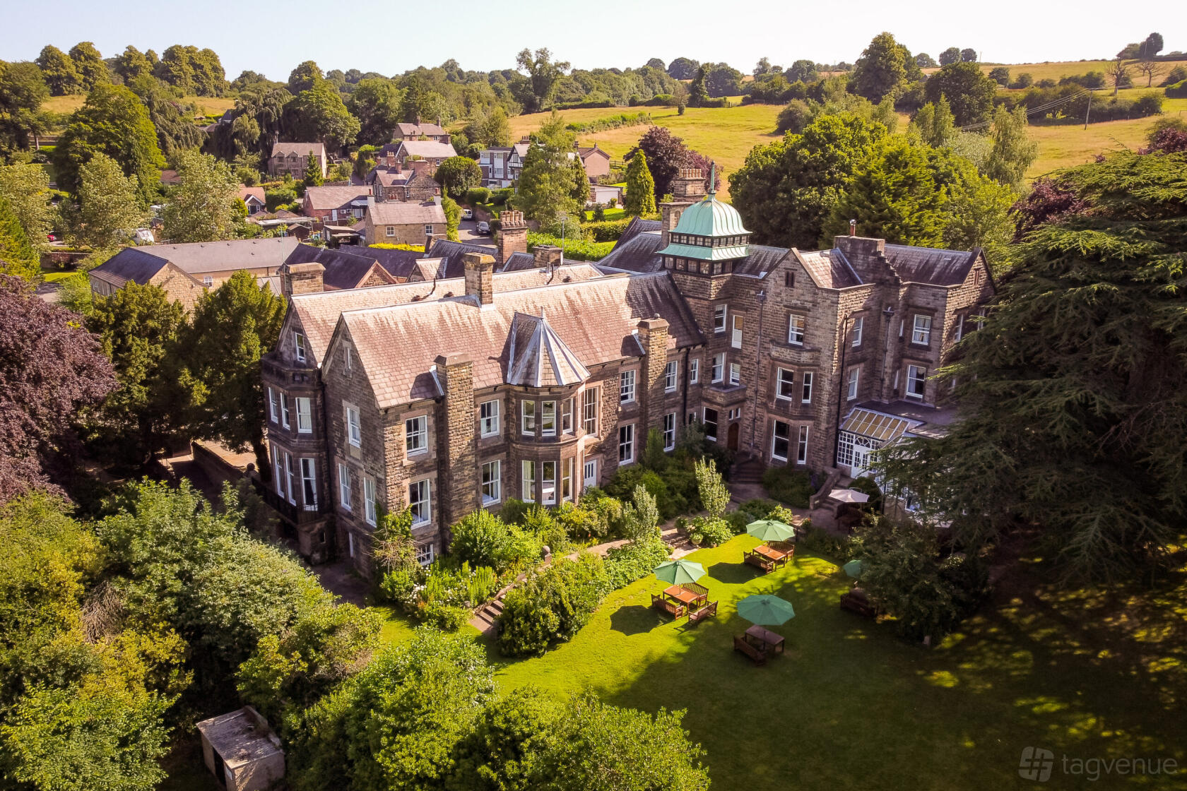 A historic hotel with stone architecture, glass conservatory, and garden seating with umbrellas at Makeney Hall Hotel.