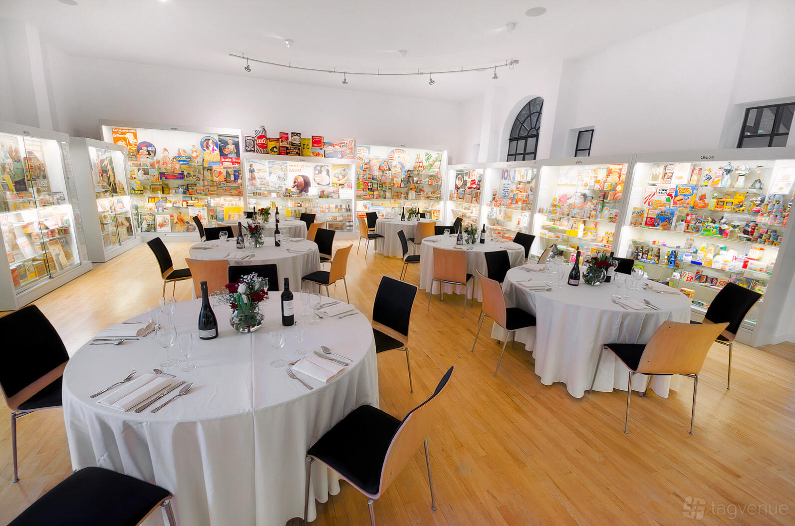 A museum event space with round tables, white linens, and illuminated display cases at Museum of Brands.