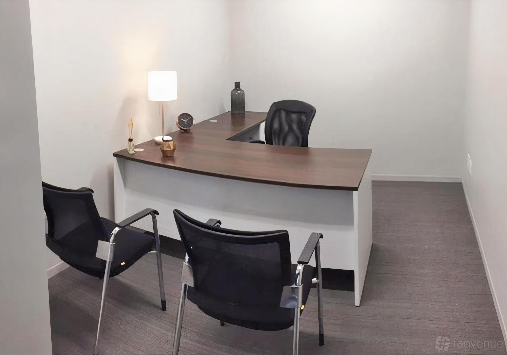 A small meeting room with a wood L-shaped desk, two guest chairs, and a desk lamp at Premier Workspaces - 2001 L STREET.