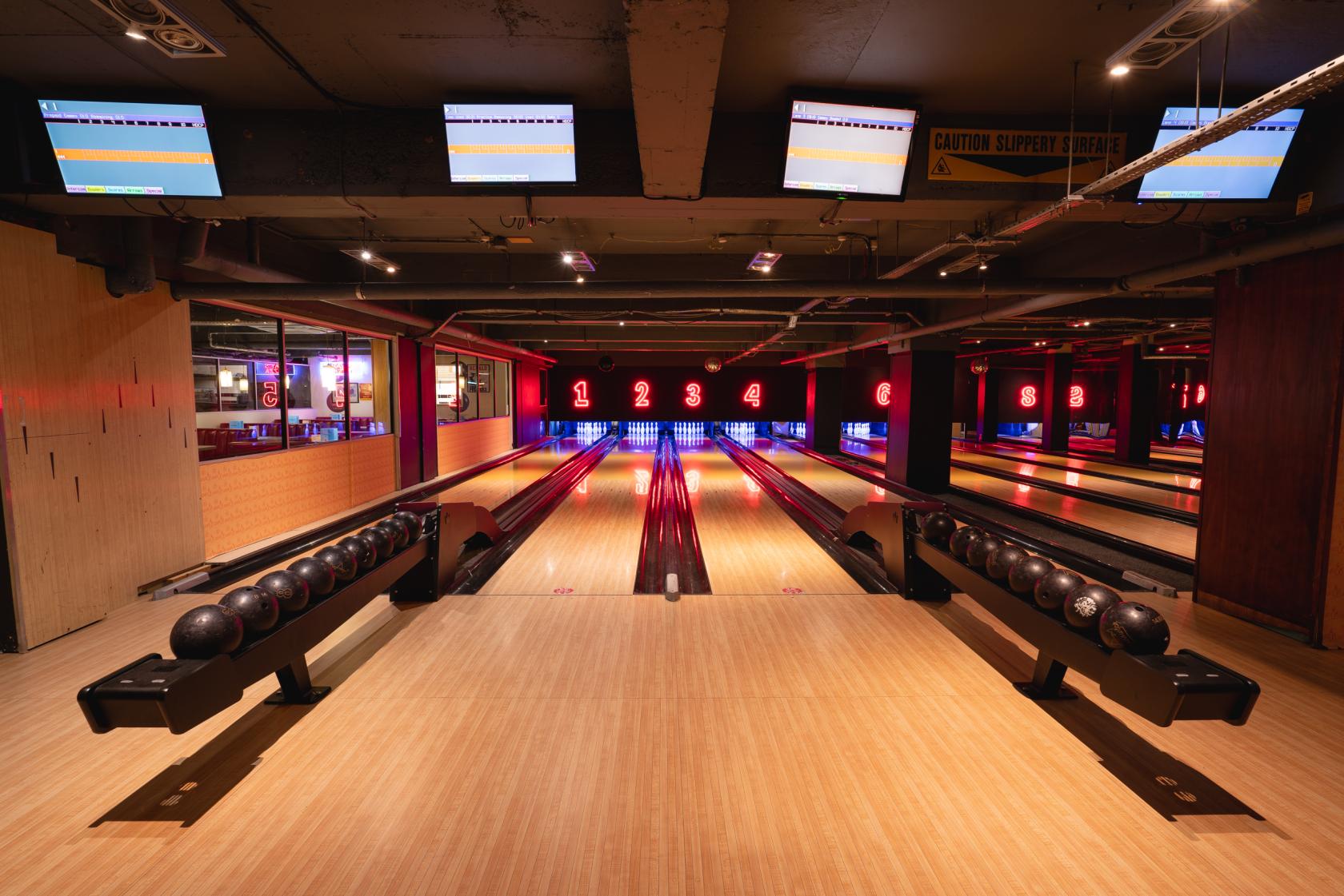 A bowling alley with multiple lanes, electronic scoreboards, and neon lane numbers at Bloomsbury Bowling Lanes & The Kingpin Suite.