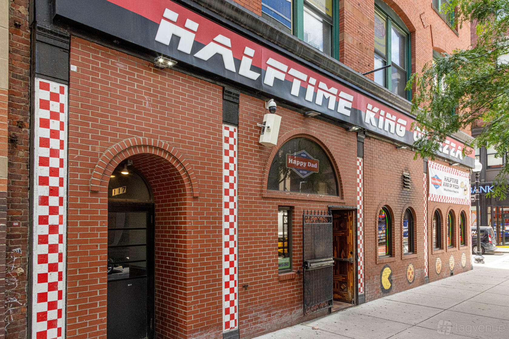 A restaurant exterior with red brick walls, checkered tile accents, arched windows, and large signage at Halftime King of Pizza.