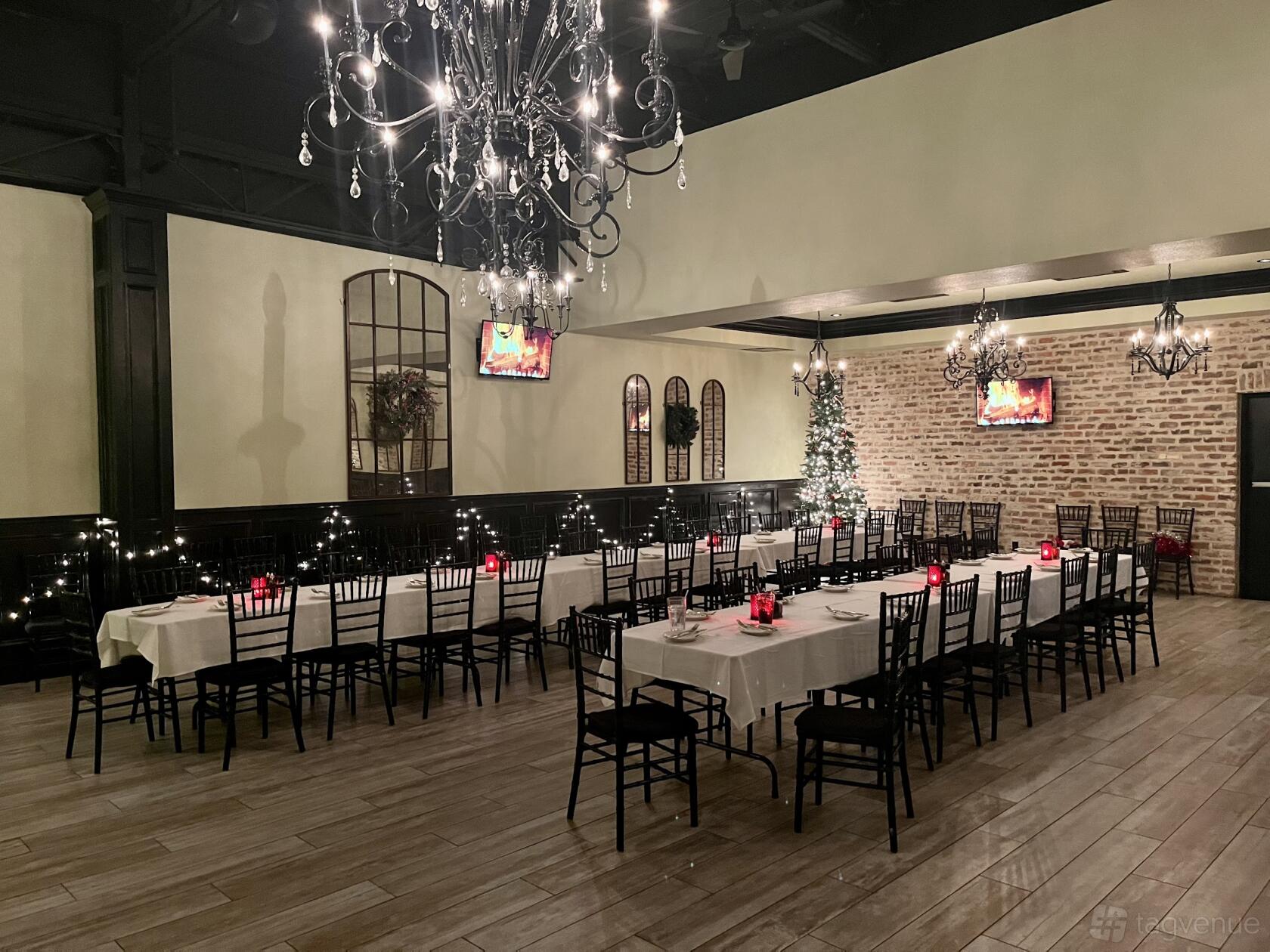 A restaurant with long banquet tables with white linens, black chairs, exposed brick walls, and chandeliers at Roman Cucina.