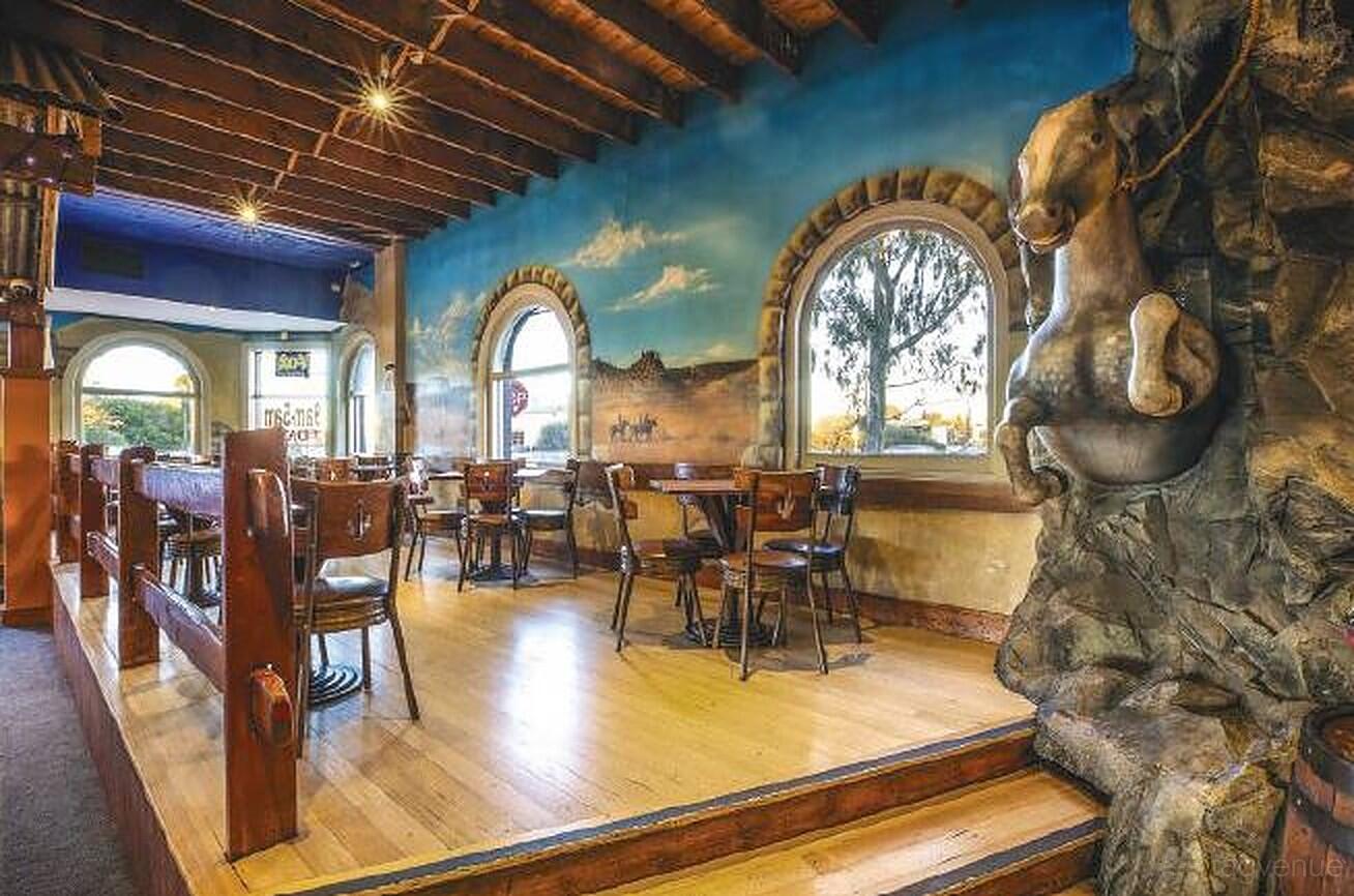 A pub interior with wooden tables, arched windows, a horse sculpture, and a painted mural at First & Last Hotel.