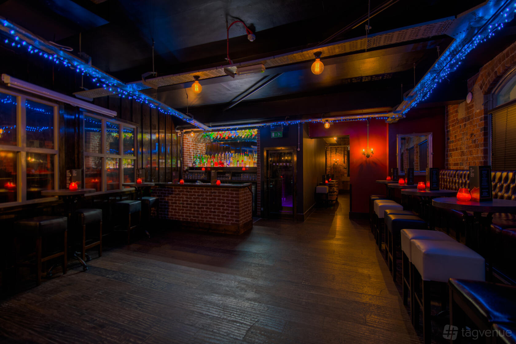 A function room in a cocktail bar with a brick bar, illuminated liquor shelves, and blue string lights at Brooklyn Bar.