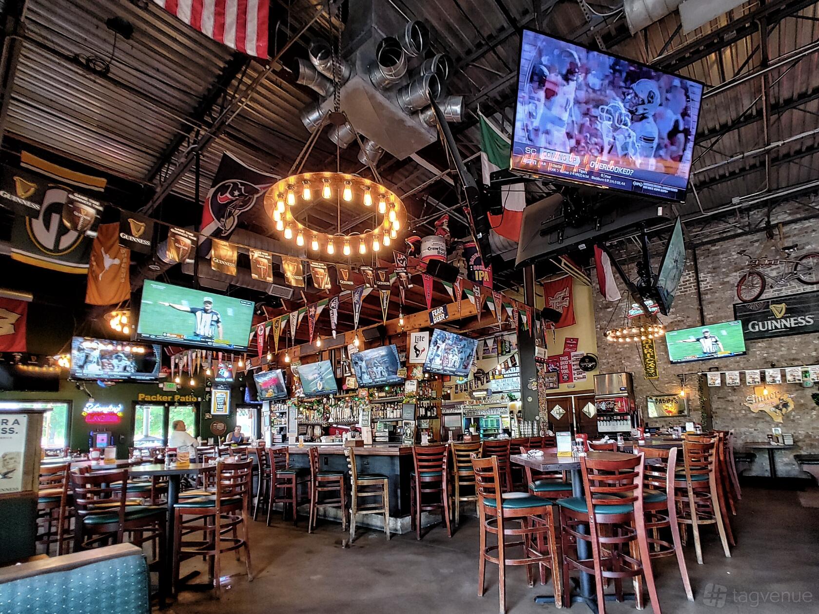 A pub with exposed brick walls, sports flags, multiple TVs, and wooden tables at Mo's Irish Pub Houston.